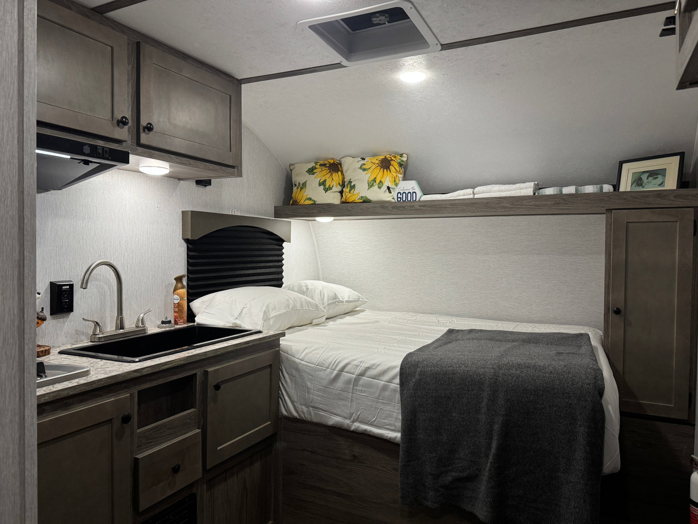 RV rental: a cozy interior featuring a bed with a grey blanket, next to a functional kitchenette with a black sink.