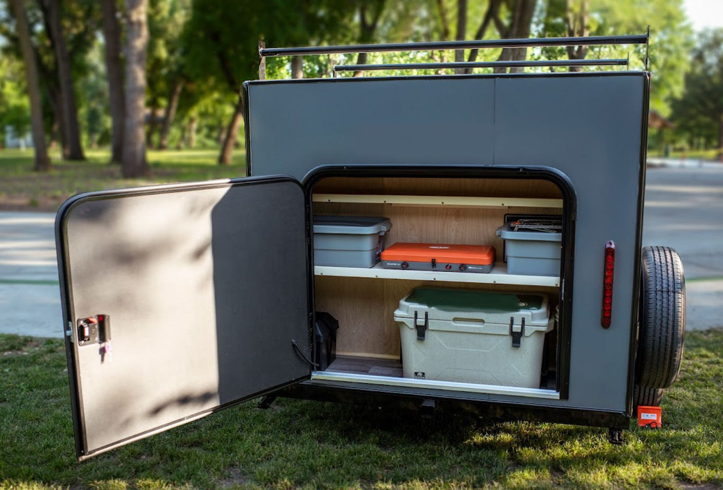 door open to reveal a bed.|Discover this compact RV rental with an open rear hatch revealing a fully equipped outdoor kitchen