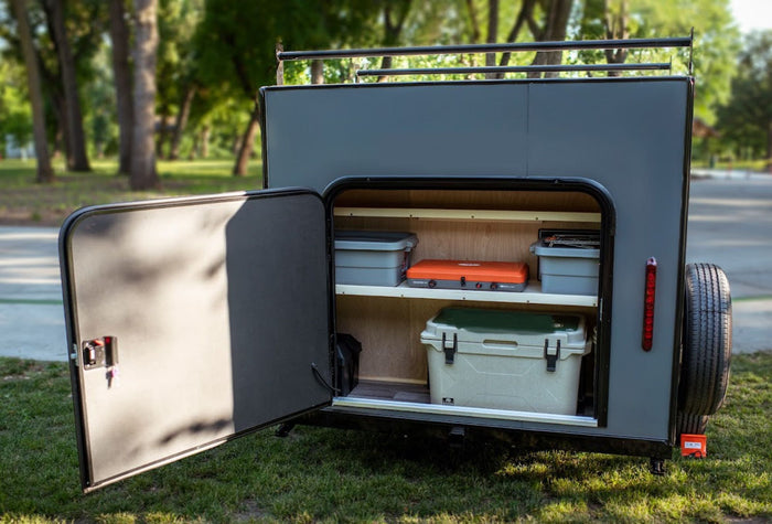 door open to reveal a bed.|Discover this compact RV rental with an open rear hatch revealing a fully equipped outdoor kitchen