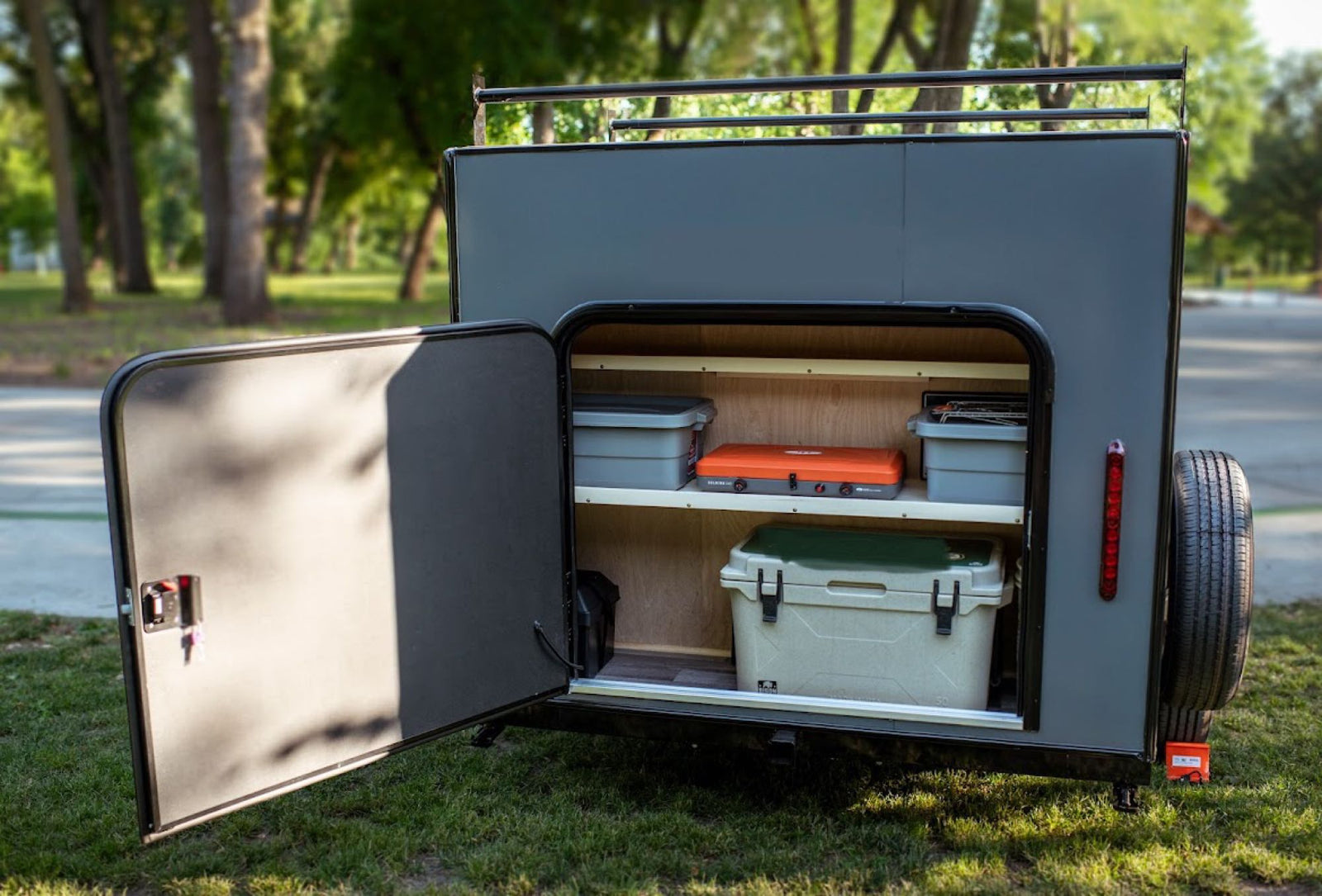 door open to reveal a bed.|Discover this compact RV rental with an open rear hatch revealing a fully equipped outdoor kitchen