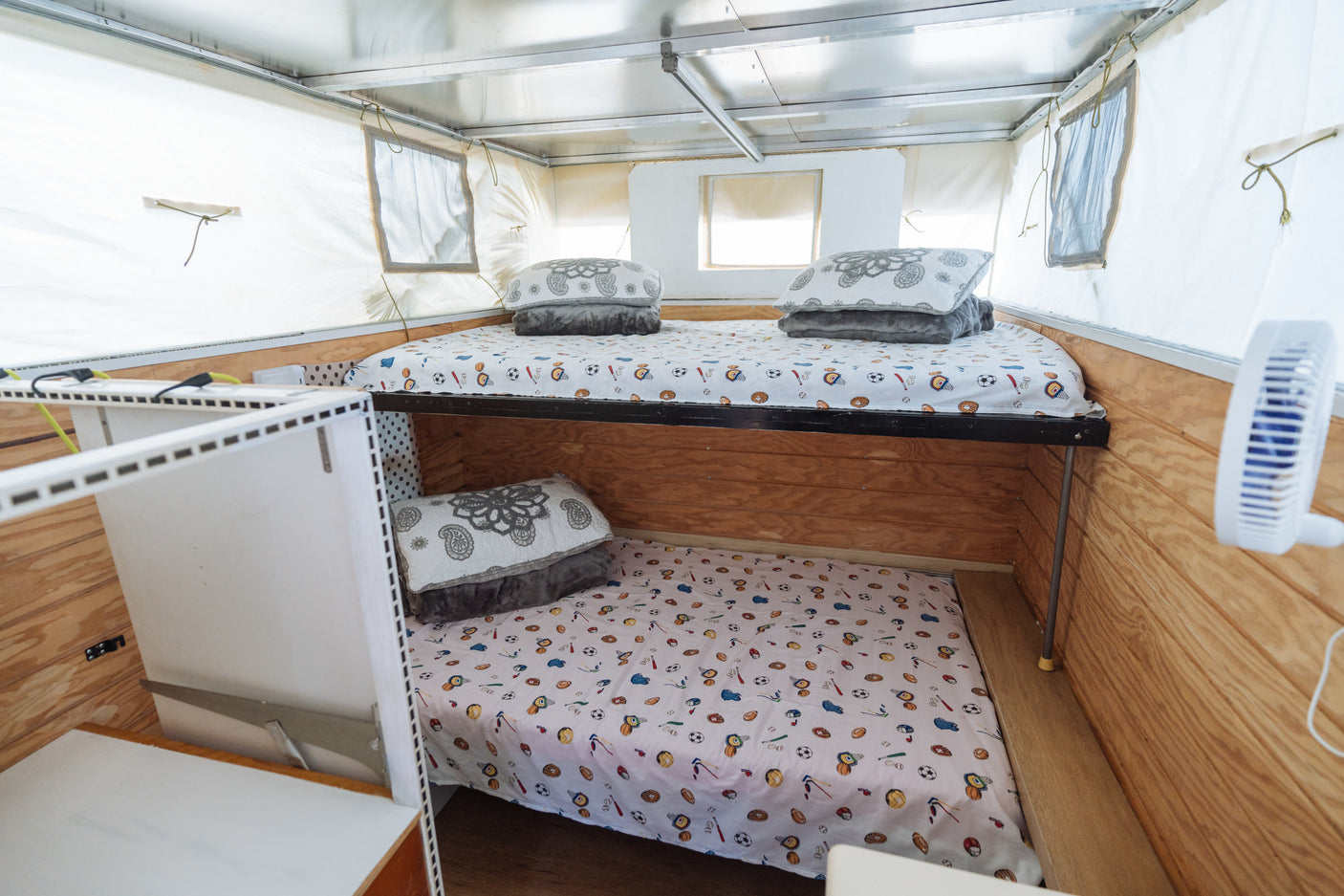 Cozy RV rental bunk beds with sports-themed bedding inside a camper. Wooden walls and a fan make it comfortable for travel.