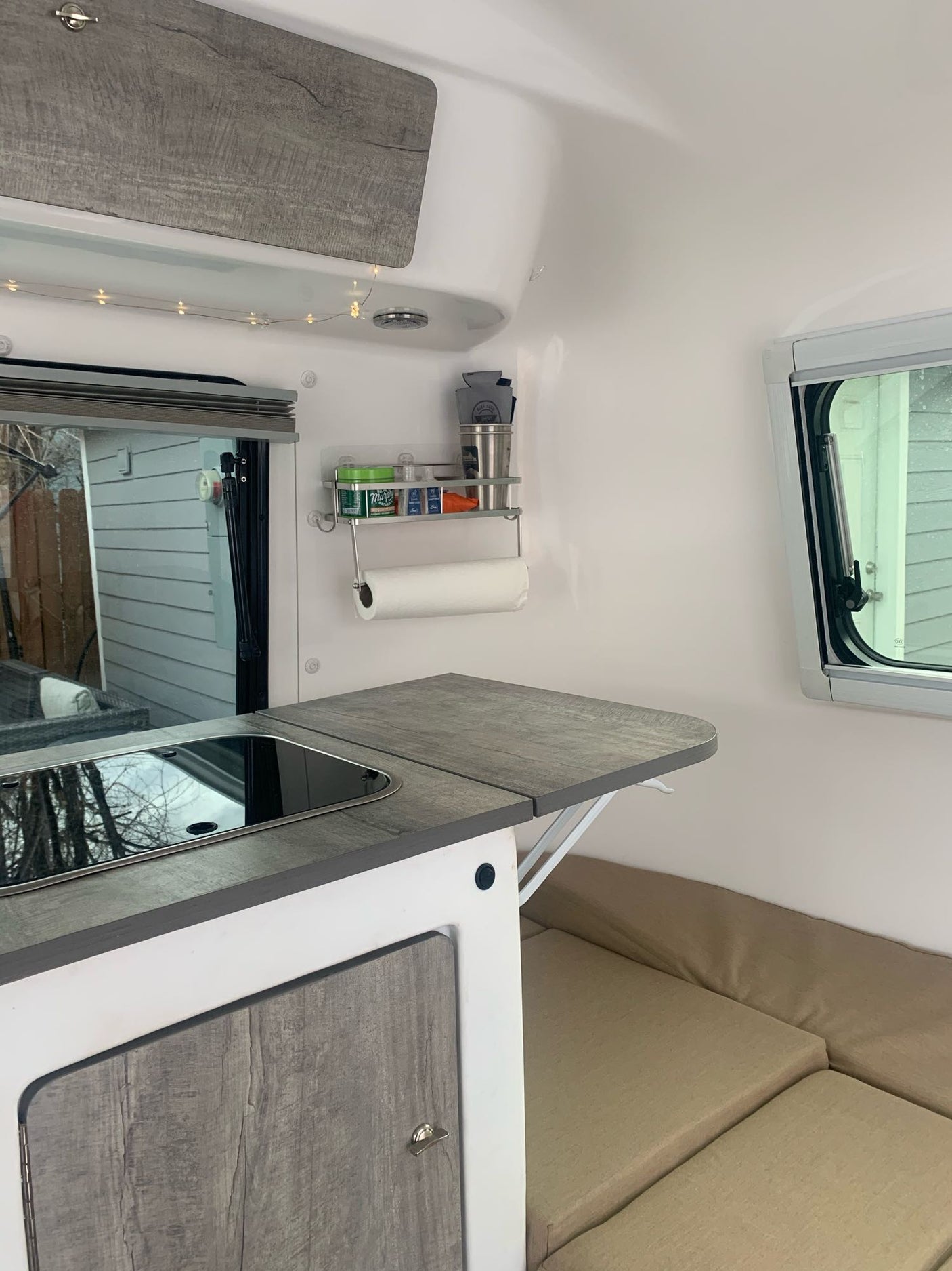 Compact RV rental interior featuring a kitchenette with integrated stovetop/sink, foldable counter, spice rack, and cozy bench seating.