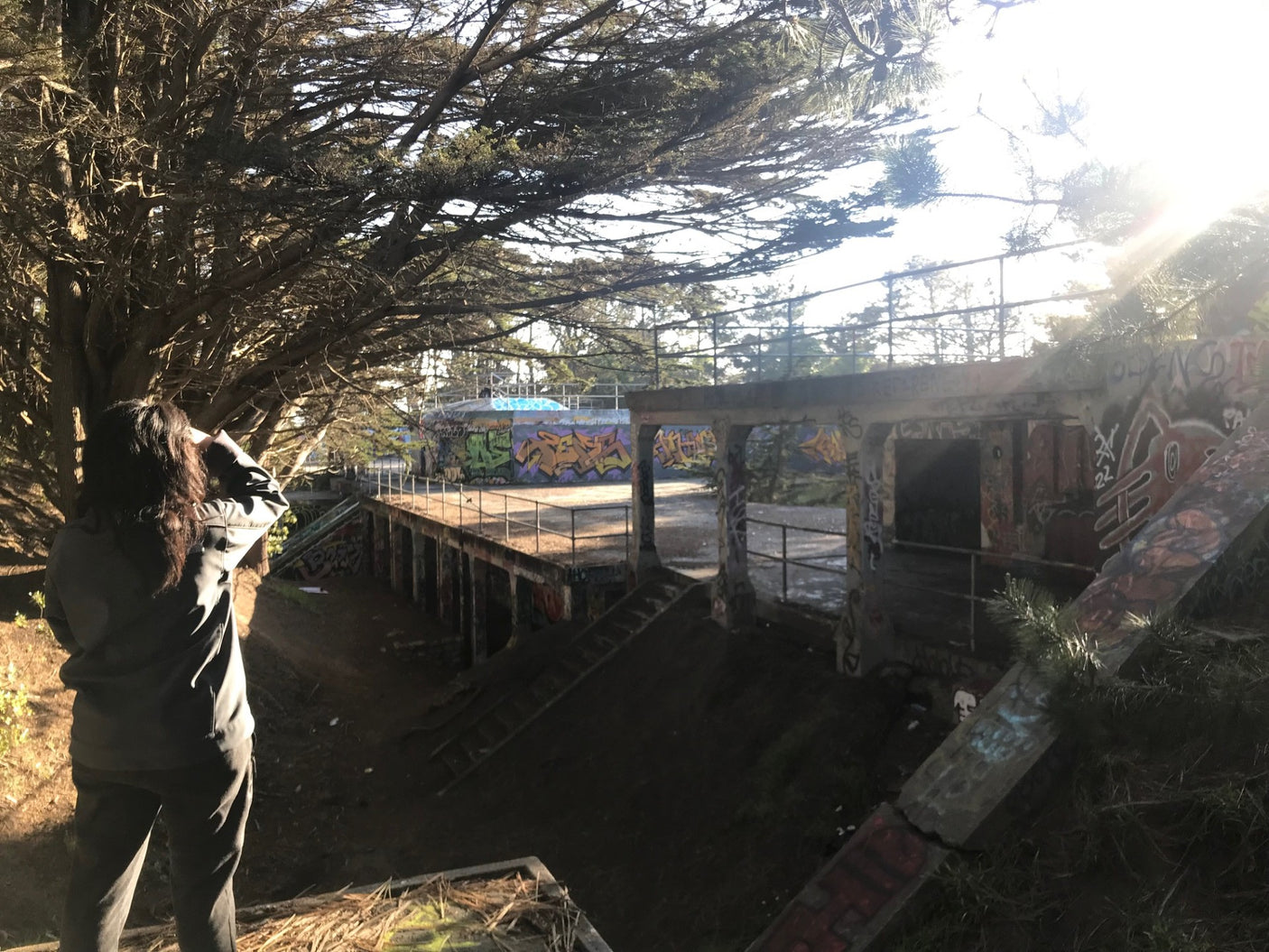 Person overlooking graffiti-covered concrete ruins & dense trees, bathed in sunlight. A unique RV rental exploration spot!