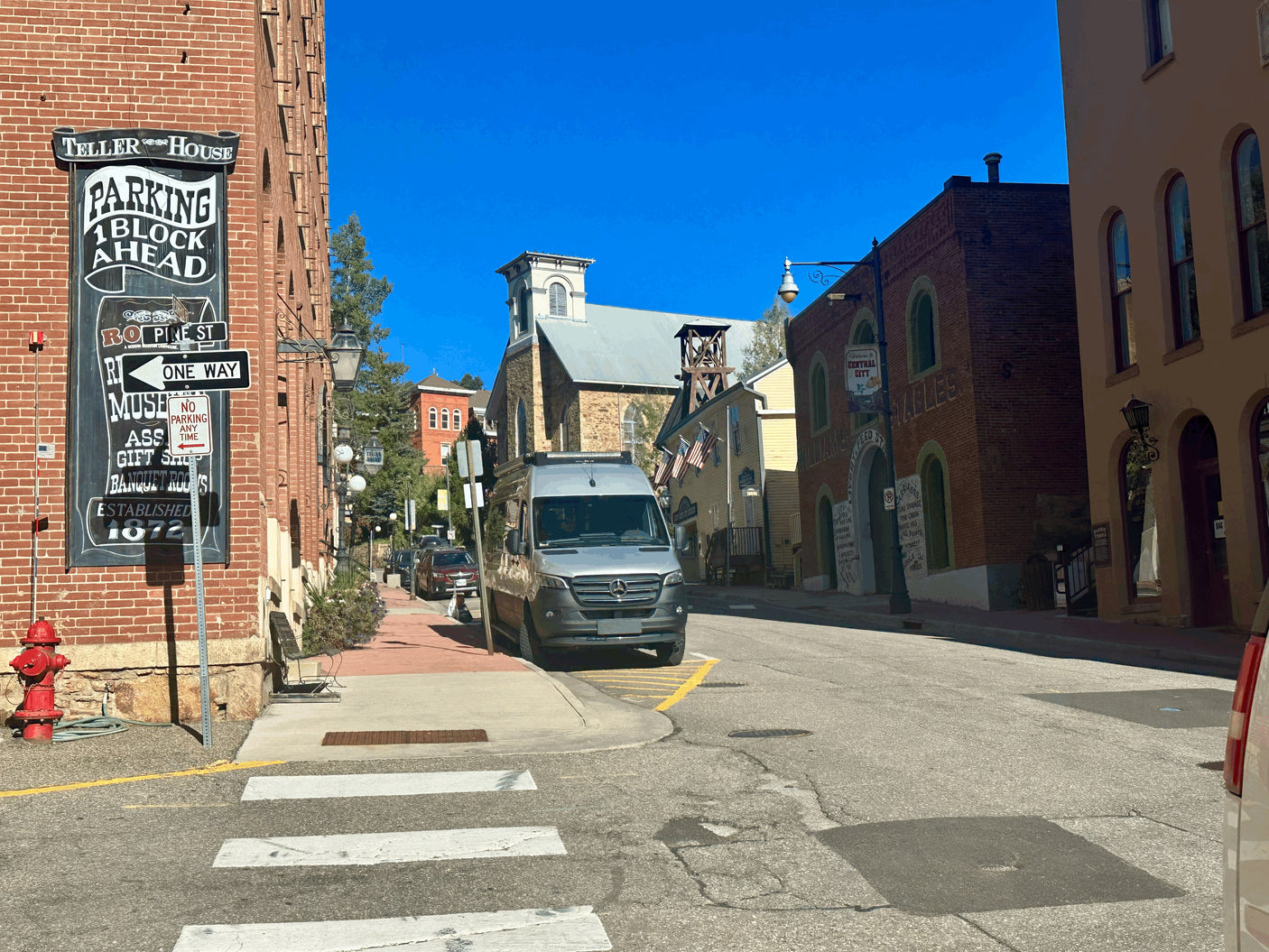 A silver RV rental van is parked on a vibrant historic street with brick buildings under a clear blue sky in Central City.