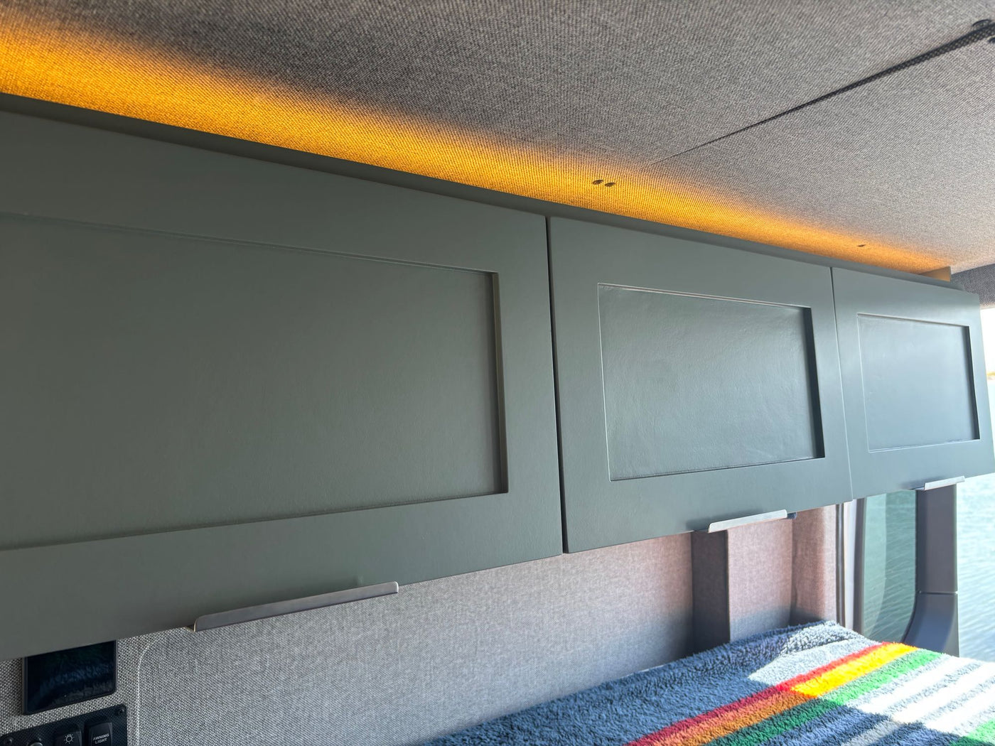 offering a stunning beach view from the sleeping area.|Cozy rv rental camper van interior with colorful bed blankets and a serene bay view from the rear.|An RV rental interior features a black foldable seat/bed mechanism stowed — photo 10