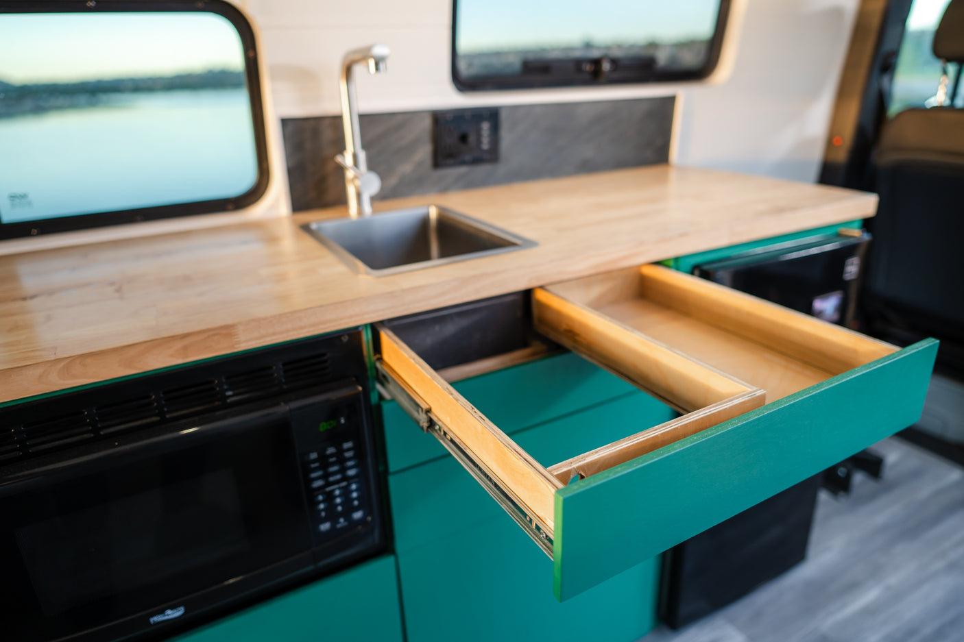 Bright RV rental kitchen featuring a wood counter, sink, built-in microwave, and practical pull-out storage.
