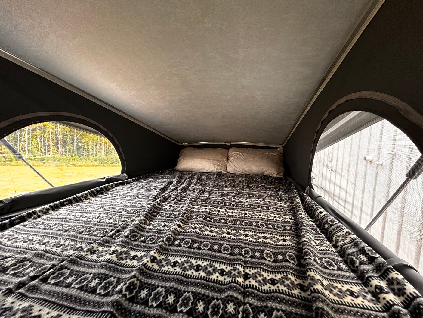 Experience comfort in this RV rental! A pop-top camper bed with a patterned blanket, pillows, and views of nature.