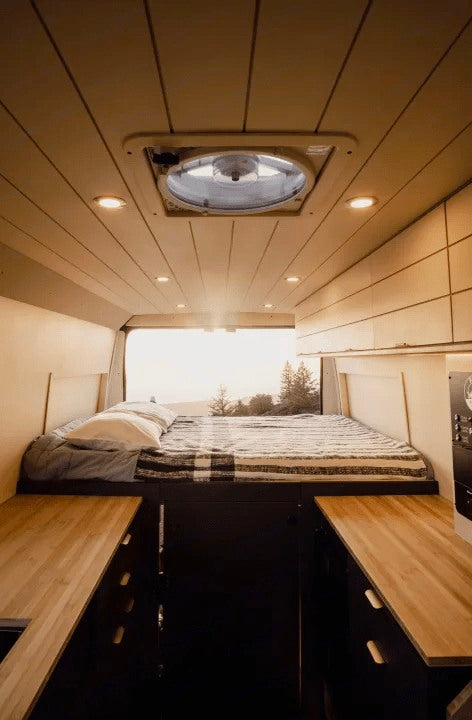 Cozy campervan rv rental interior: elevated bed with nature views, wood-paneled ceiling, fan, and compact kitchenettes.