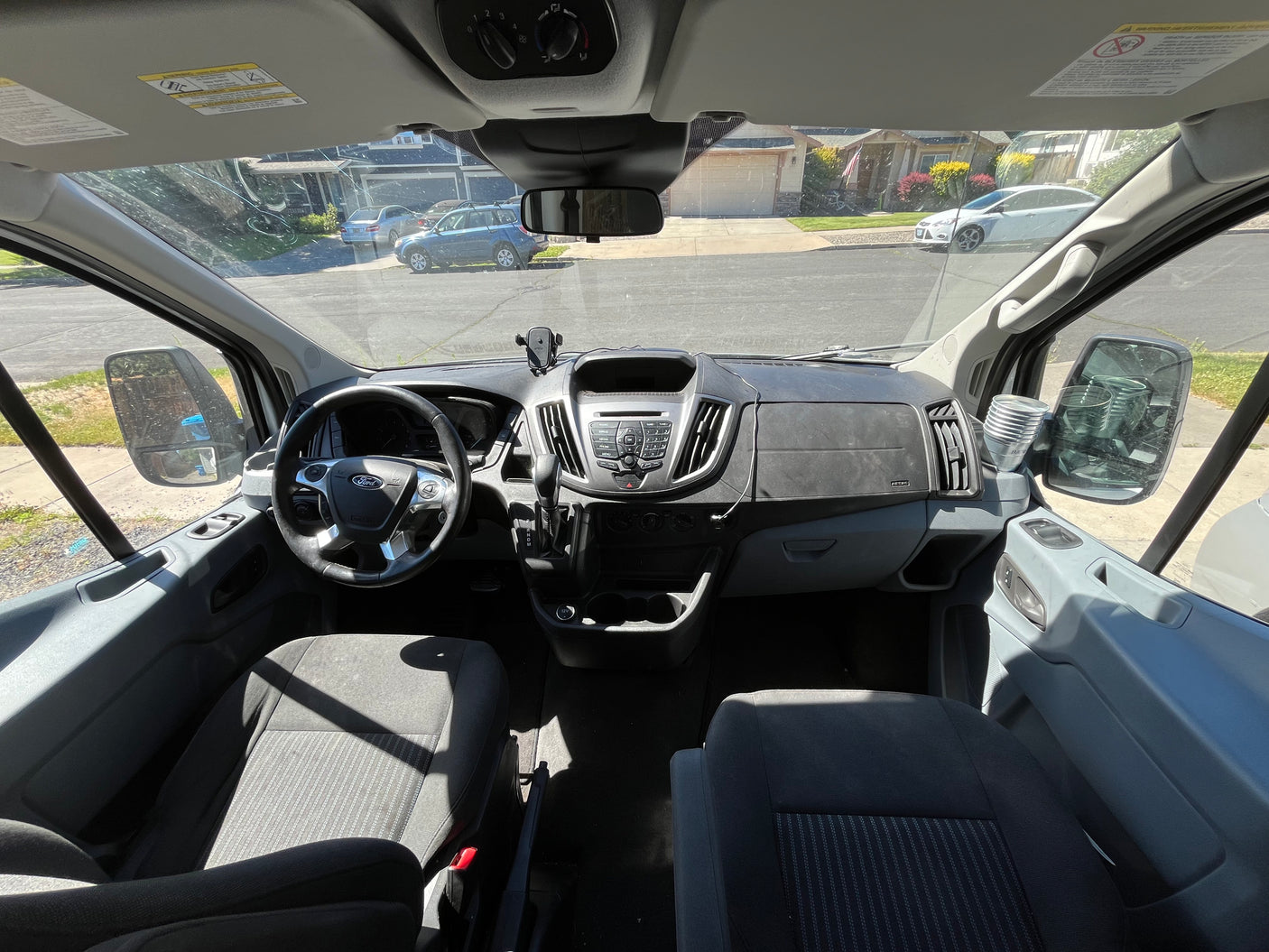 RV rental van interior: Driver's cockpit with Ford steering wheel, dashboard, and outside street view through the windshield.