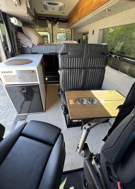 View inside an RV rental, featuring a bed, kitchen with fridge, and modular seating with a table.