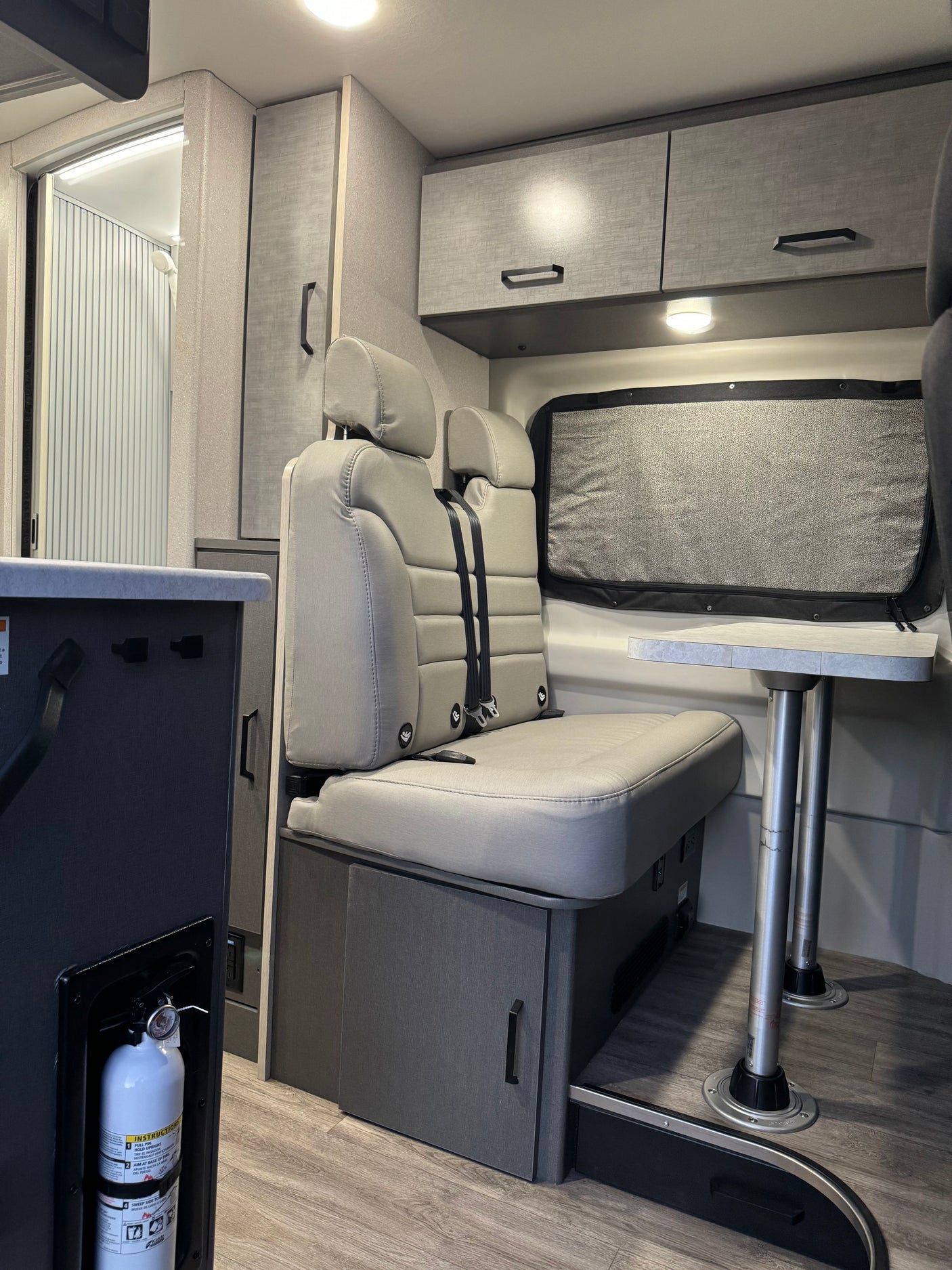 RV rental: Bright interior featuring light gray dinette seating, overhead cabinets, a versatile table, and shower access.