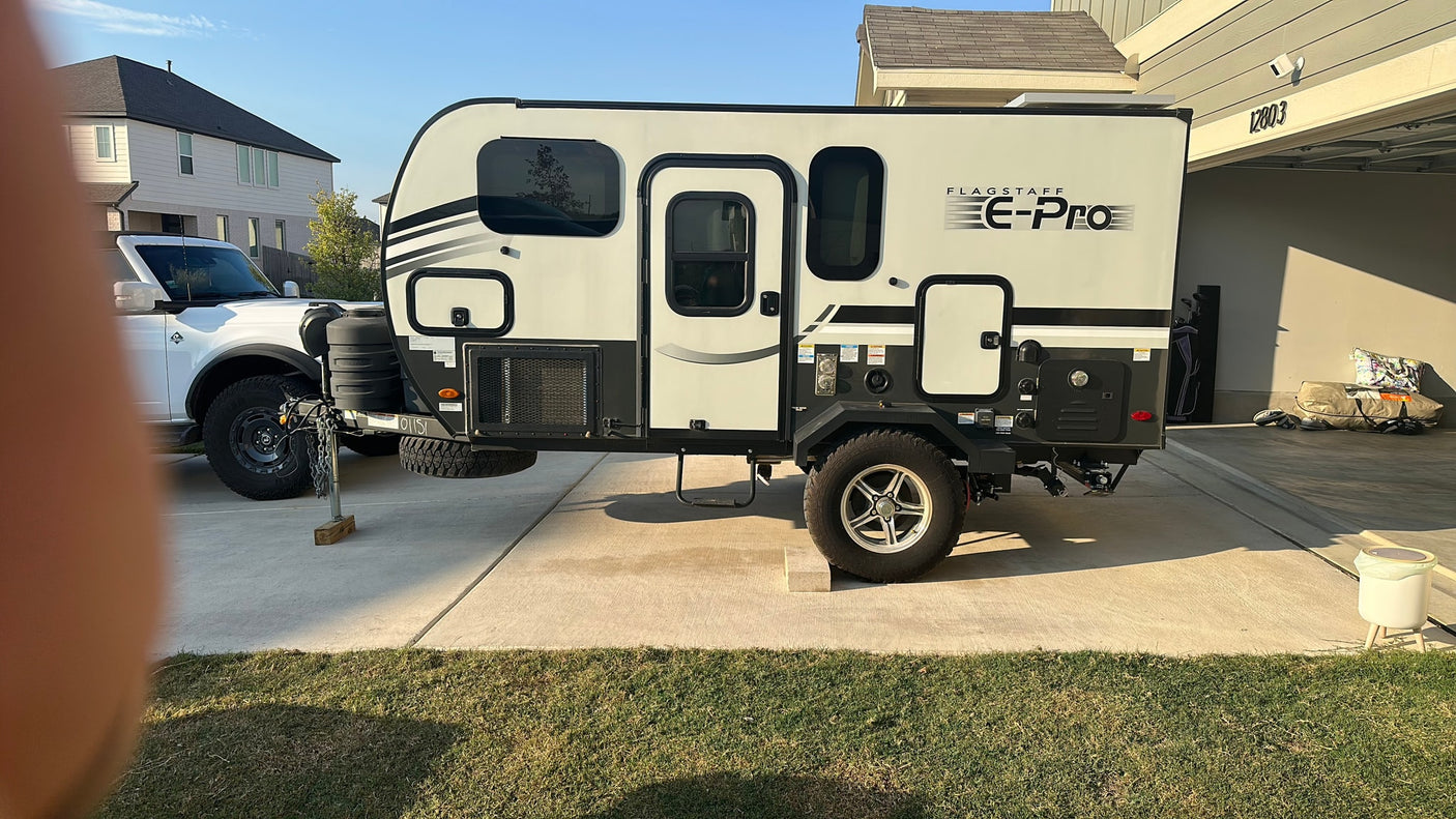 A compact, modern Flagstaff E-Pro travel trailer, ideal for rv rental, parked on a sunny residential driveway near a white truck.