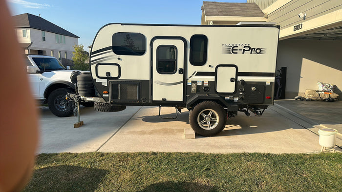 A compact, modern Flagstaff E-Pro travel trailer, ideal for rv rental, parked on a sunny residential driveway near a white truck.