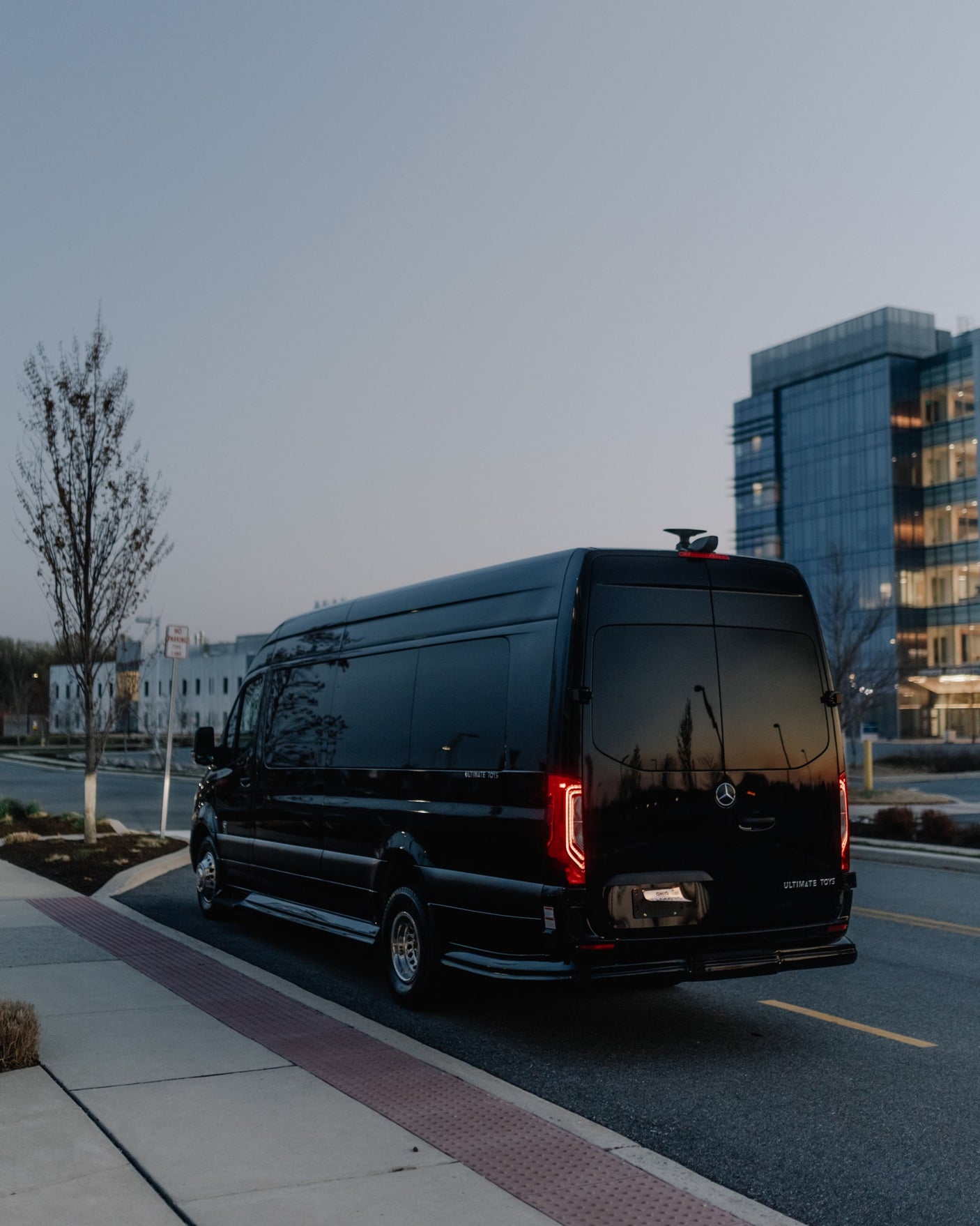 Black Mercedes-Benz Sprinter luxury van by Ultimate Toys, an Ohio RV rental, parked at dusk near modern buildings.