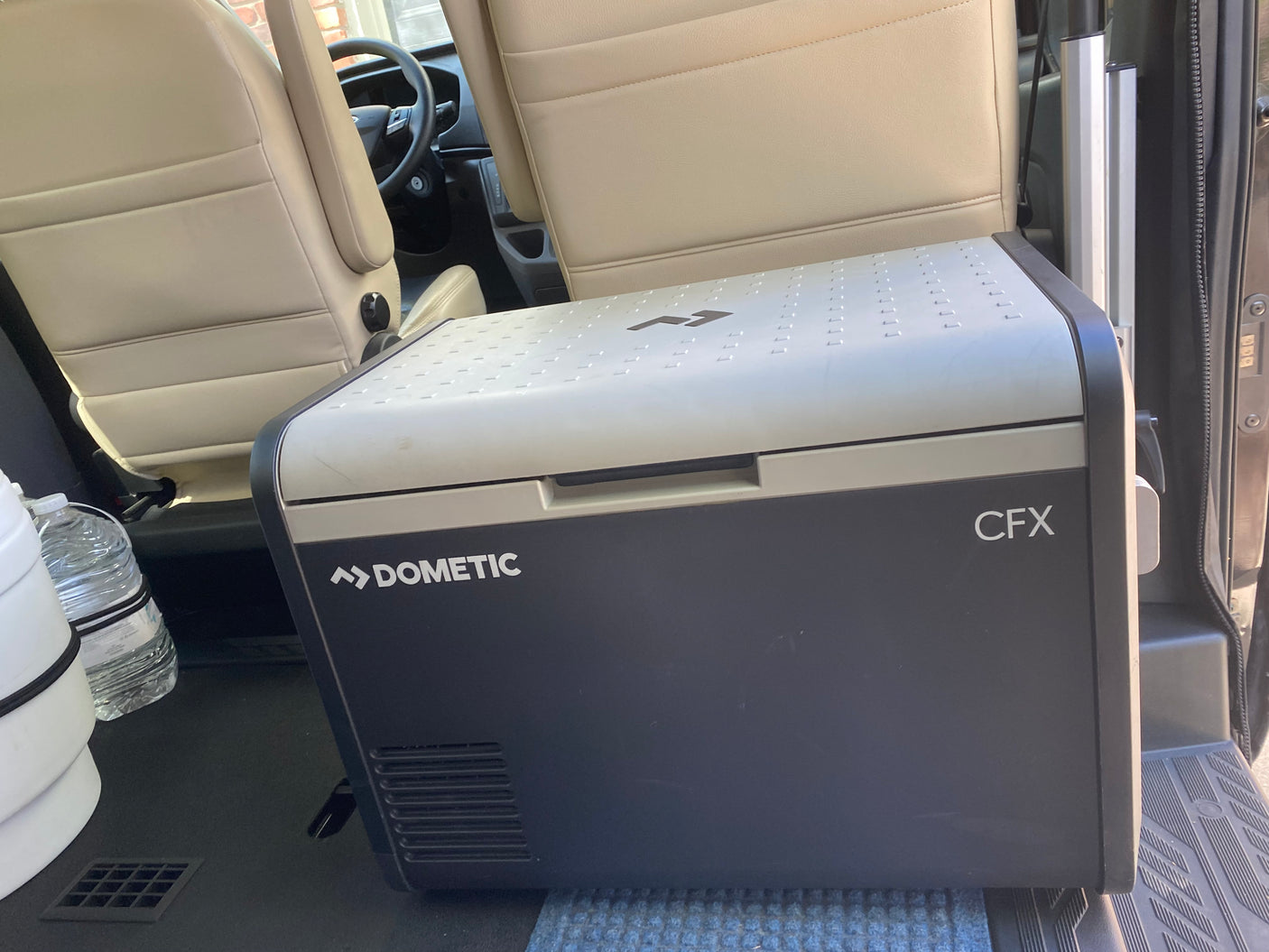 A Dometic CFX portable cooler rests inside an RV rental, positioned near passenger seats for travel.