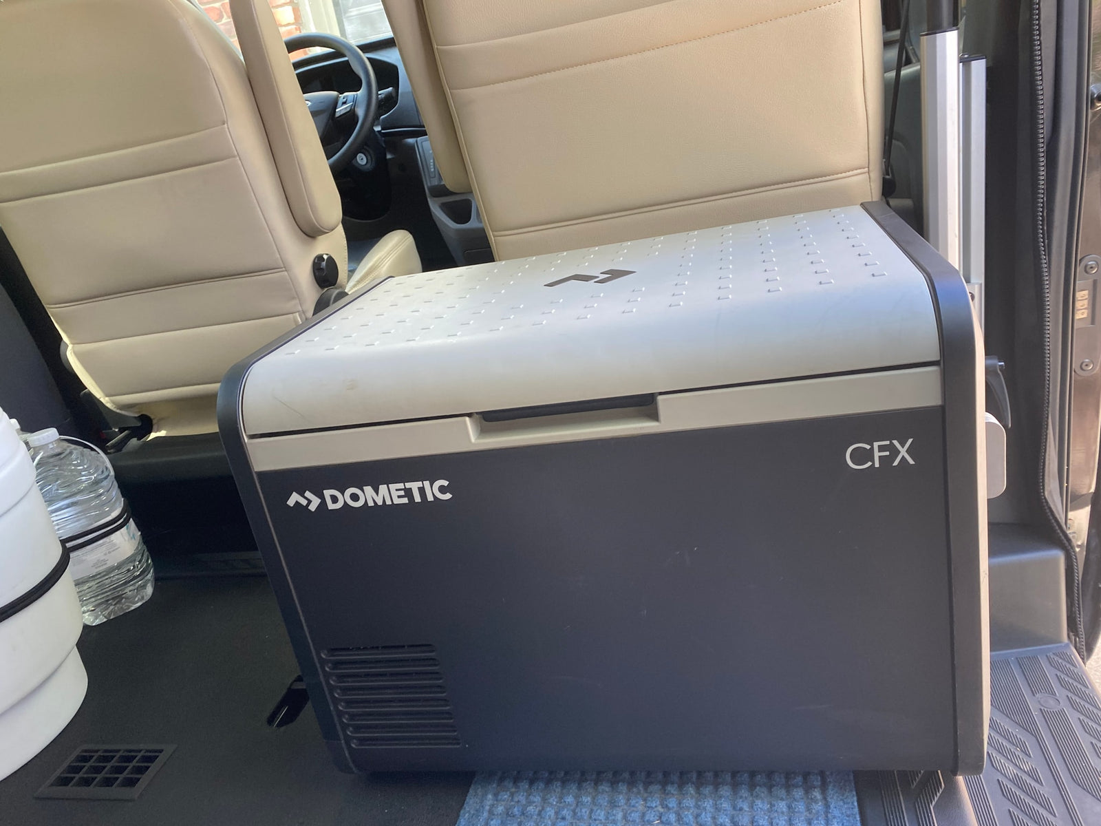 A Dometic CFX portable cooler rests inside an RV rental, positioned near passenger seats for travel.
