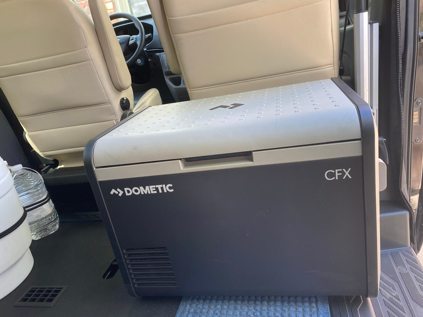 A Dometic CFX portable cooler rests inside an RV rental, positioned near passenger seats for travel.
