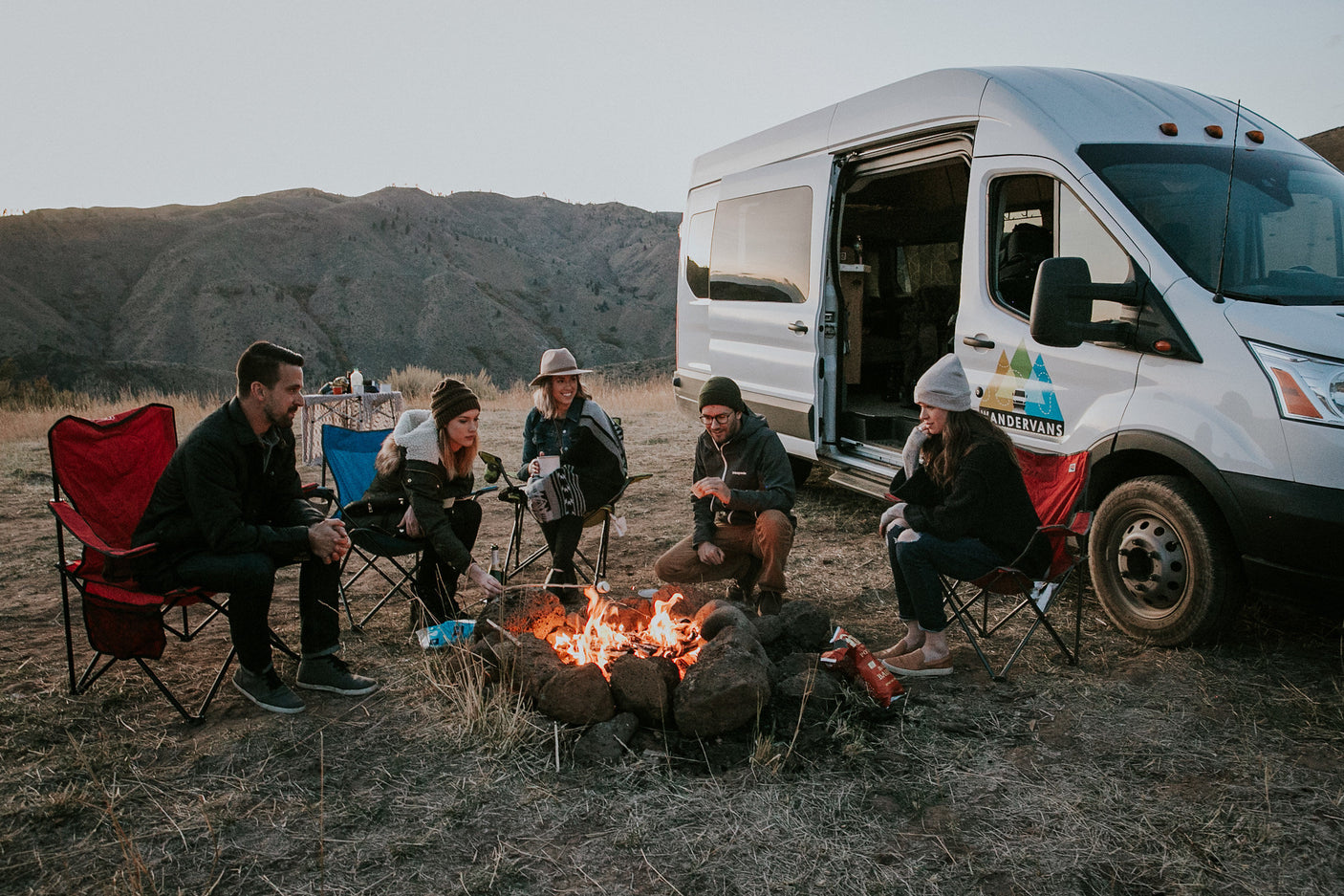 Friends gather around a campfire, roasting marshmallows, enjoying their RV rental van camping.