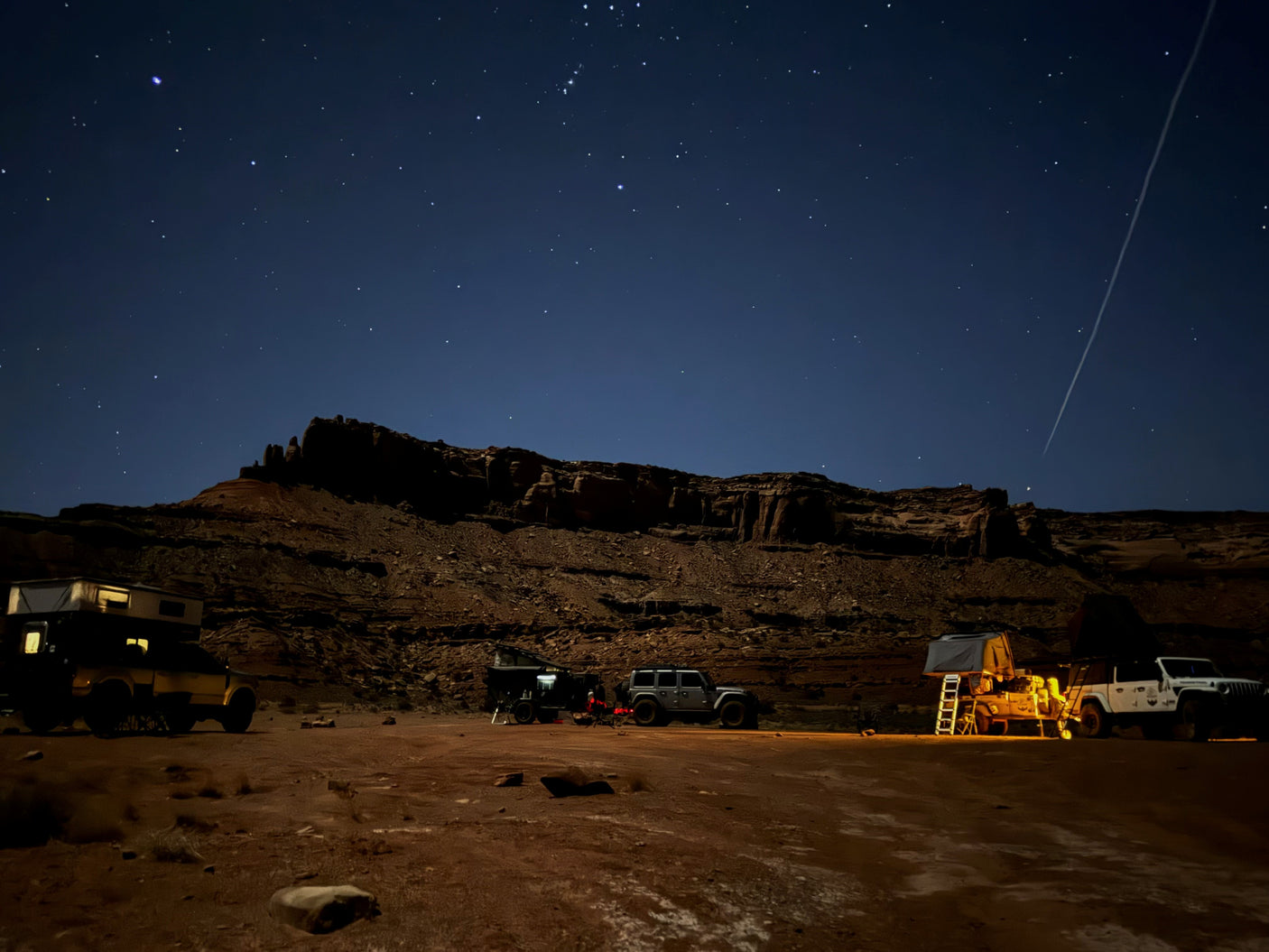 Starry desert night: Jeeps, truck w/ camper, & trailer w/ tent at an overland camp. Experience this adventure with an RV rental!