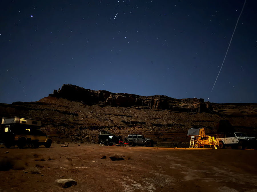 Starry desert night: Jeeps, truck w/ camper, & trailer w/ tent at an overland camp. Experience this adventure with an RV rental!