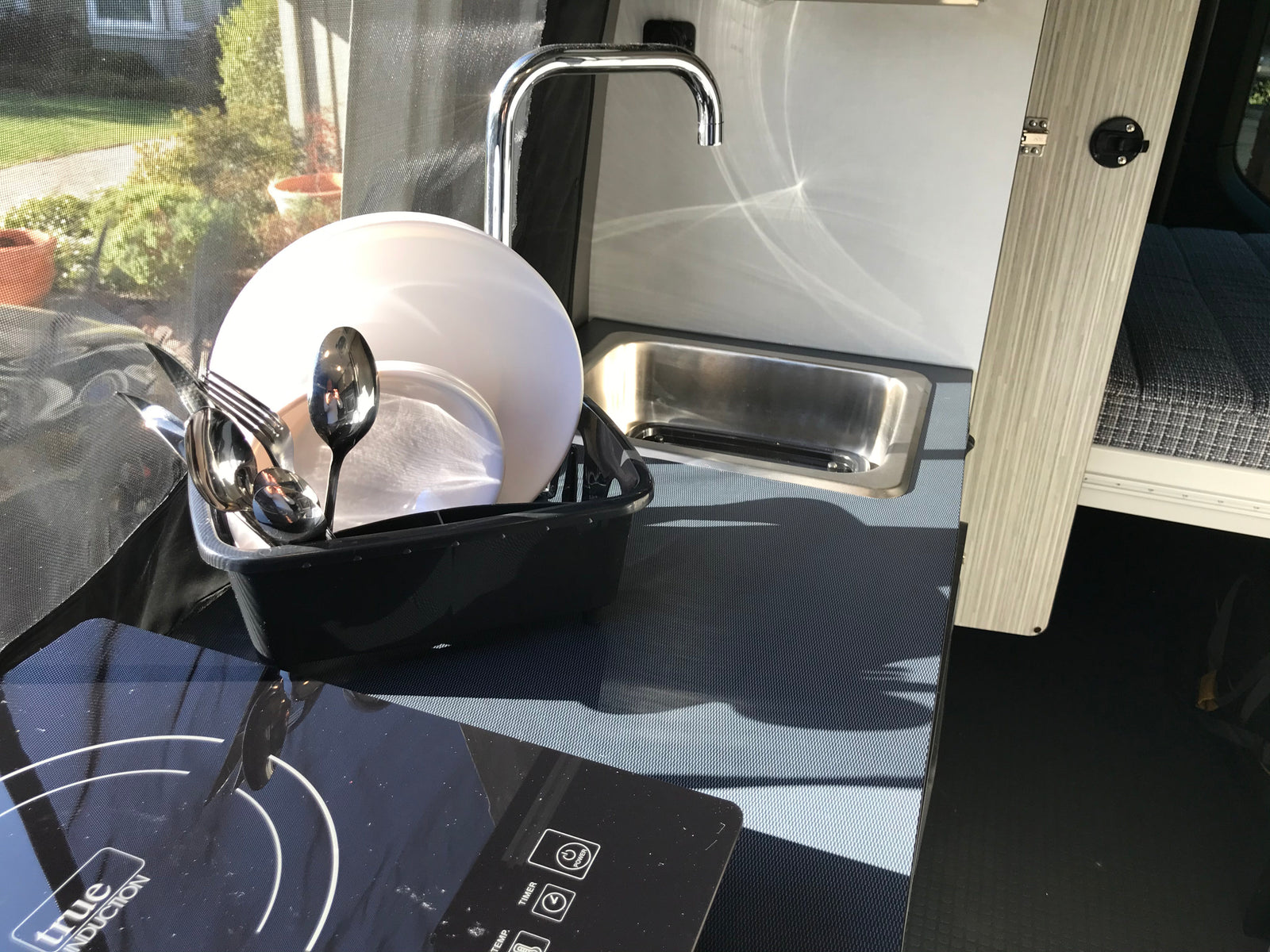 Enjoy an RV rental's functional mobile kitchen with induction cooktop, sink, and dish drying rack for convenient camping.