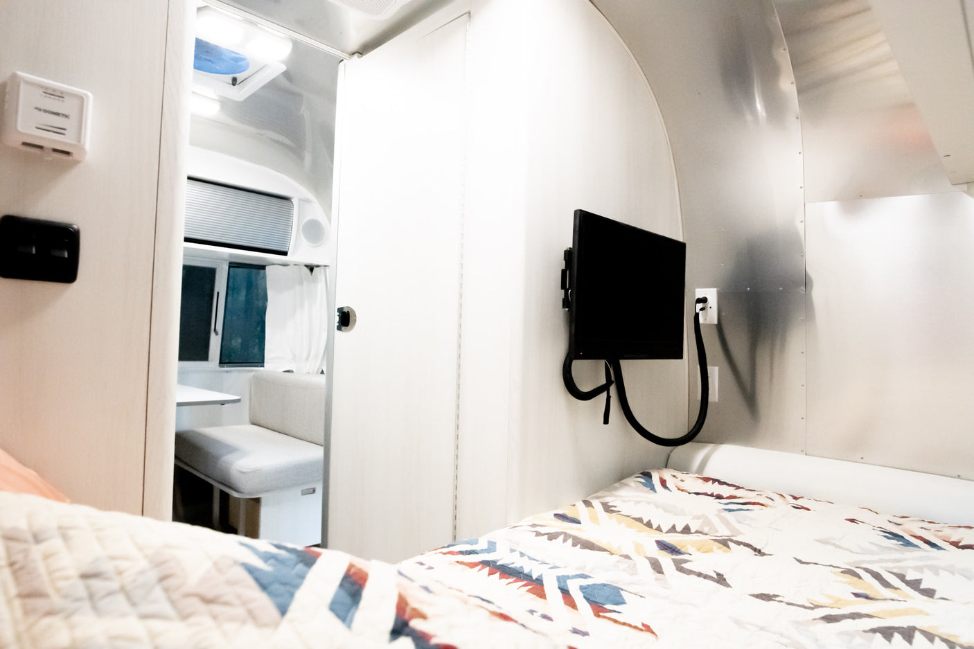 Compact RV rental interior: cozy bed, modern dinette, and entertainment for your travels.