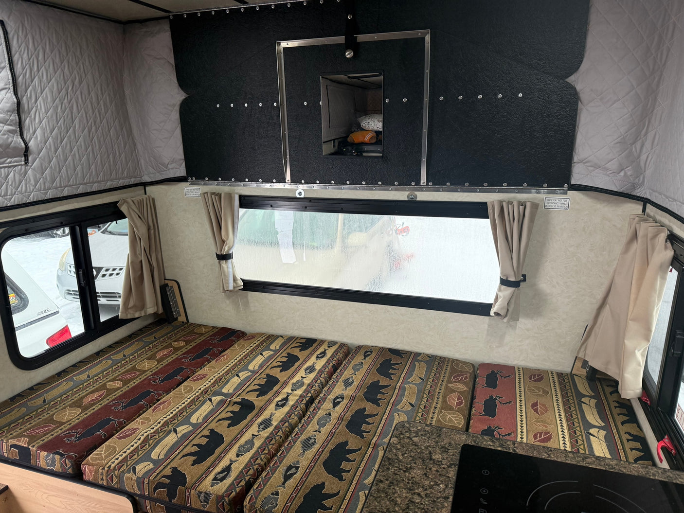 Inside an RV rental: nature-patterned cushions, pop-top walls, and a window for scenic camping views.