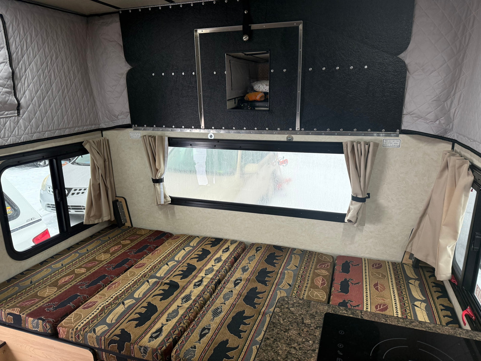 Inside an RV rental: nature-patterned cushions, pop-top walls, and a window for scenic camping views.