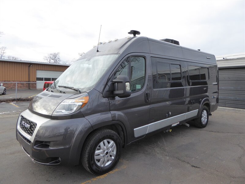 an ideal rv rental for spacious travel adventures.|This gray Ram ProMaster camper van is ready for your next rv rental adventure. It's parked on asphalt in front of buildings.|Dark grey camper van for rv rental