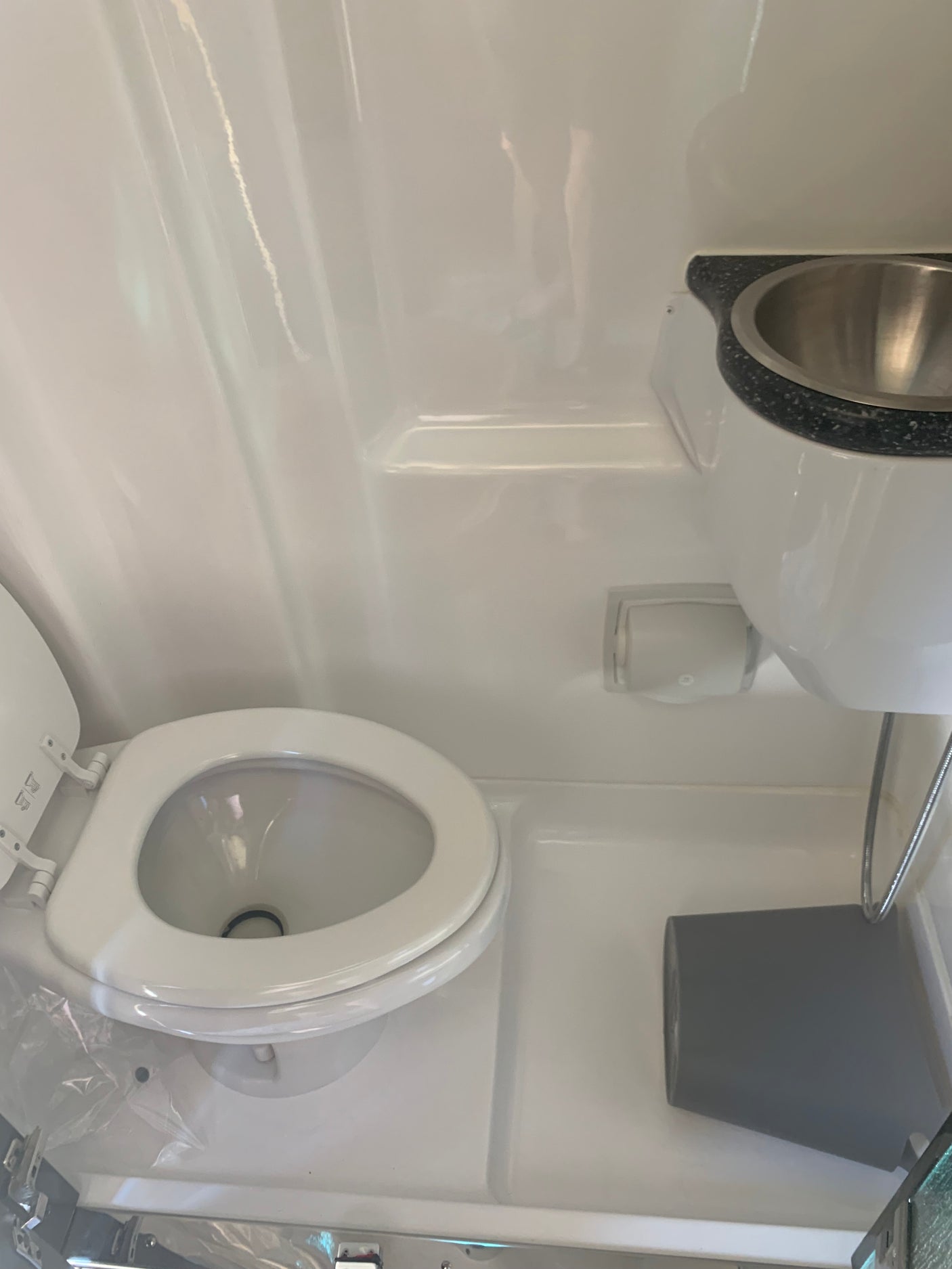 Compact rv rental bathroom featuring a white toilet with open lid, overhead sink, and hanging storage bin.