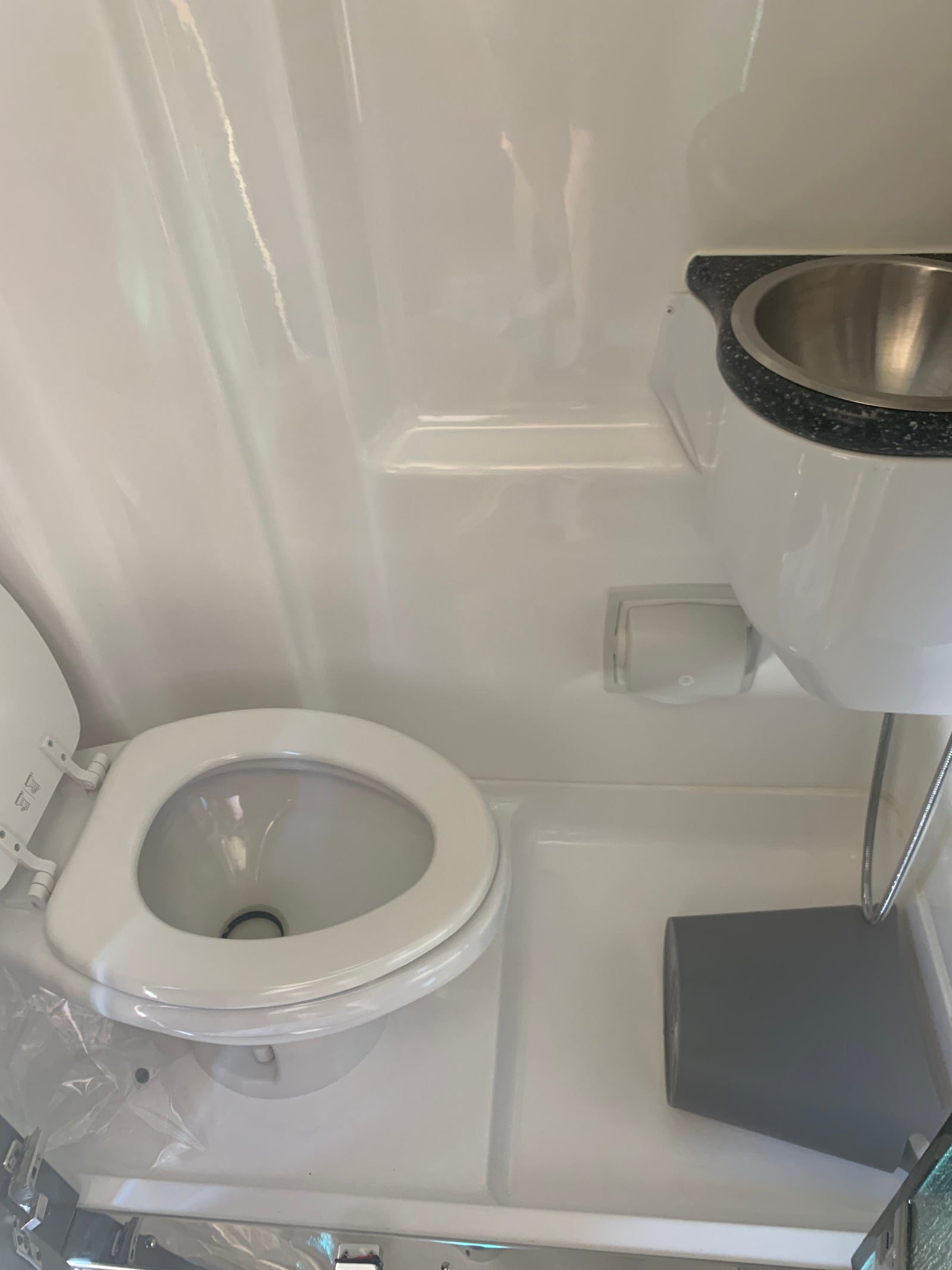 Compact rv rental bathroom featuring a white toilet with open lid, overhead sink, and hanging storage bin.