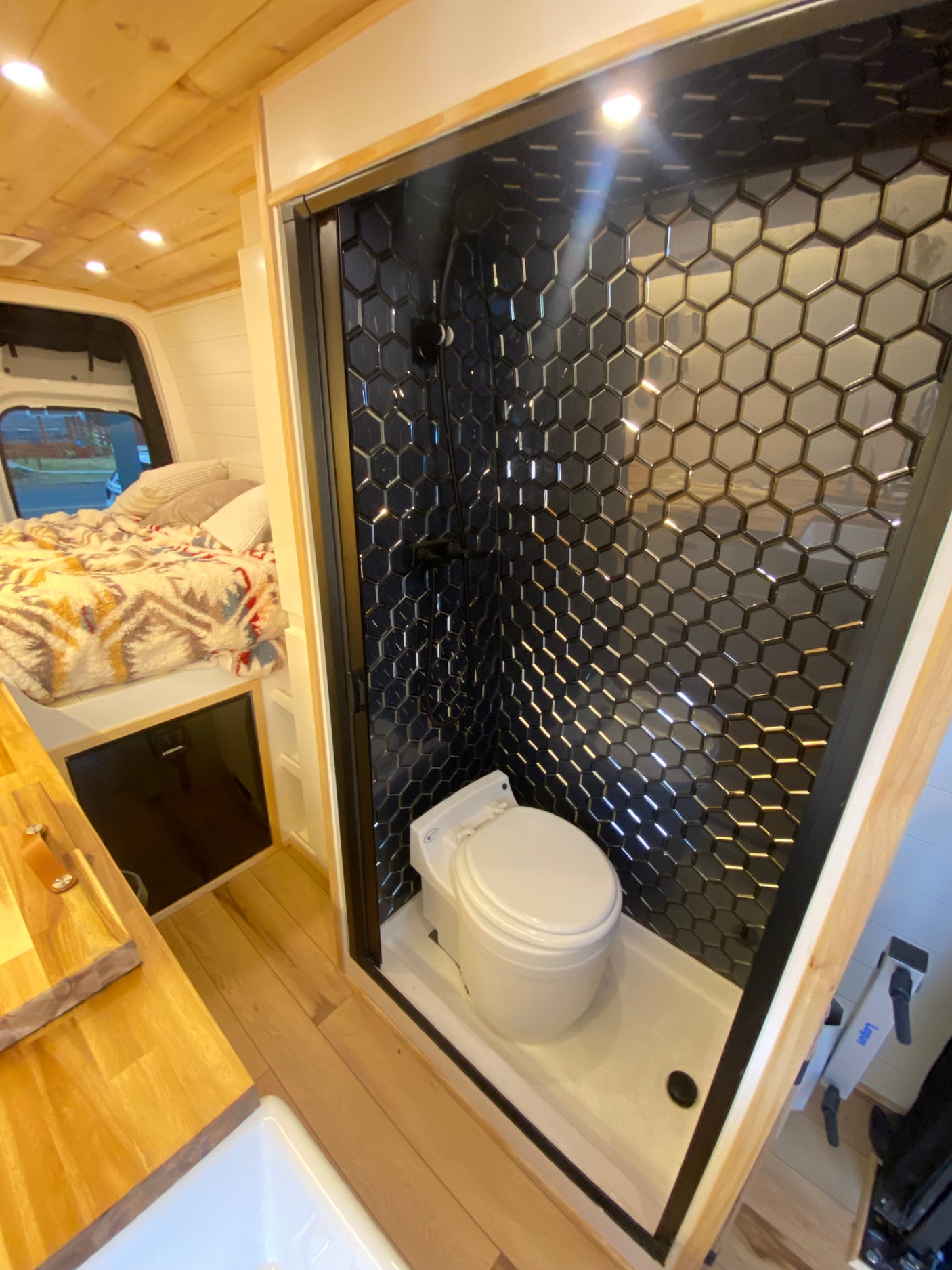 Compact RV rental interior with a chic hexagon-tiled shower/toilet and a comfortable bed