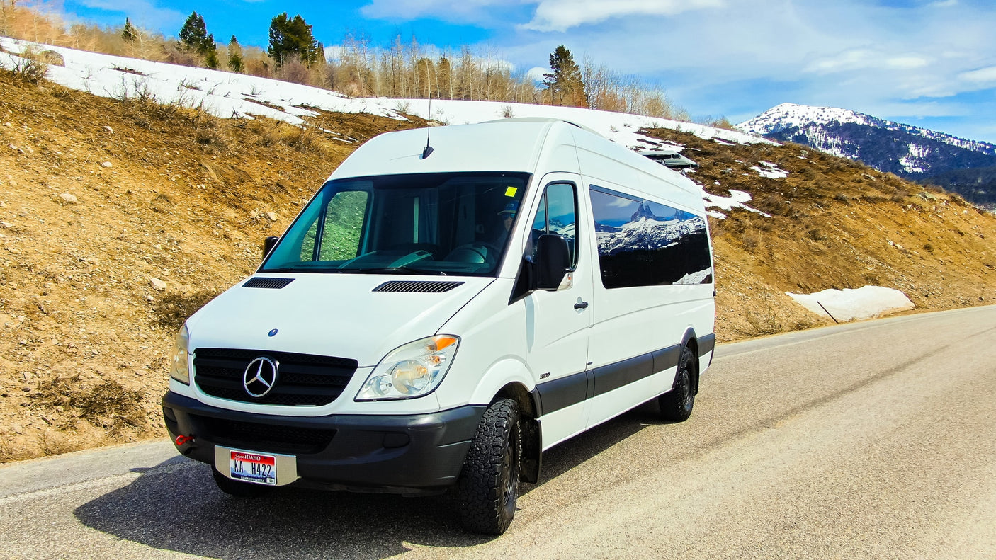 White Mercedes-Benz Sprinter camper van (RV rental) on a snowy mountain road. Ready for your next outdoor adventure.
