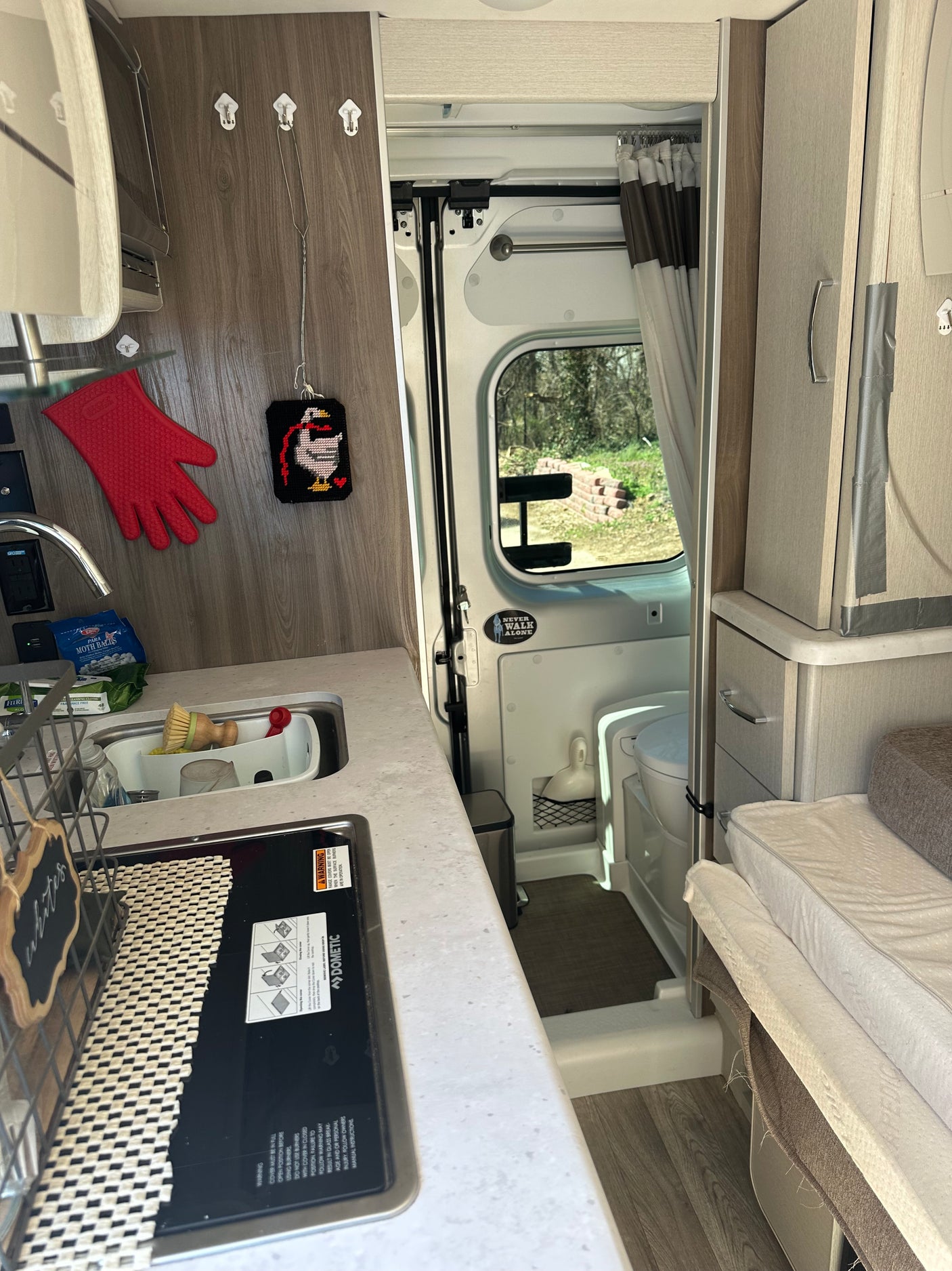 Compact RV rental interior featuring a kitchen with Dometic stove, sink, an adjacent wet bath, and seating/sleeping area.