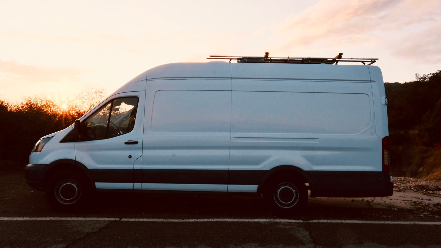 RV rental: White camper van with a roof rack, parked on a roadside at scenic sunset.