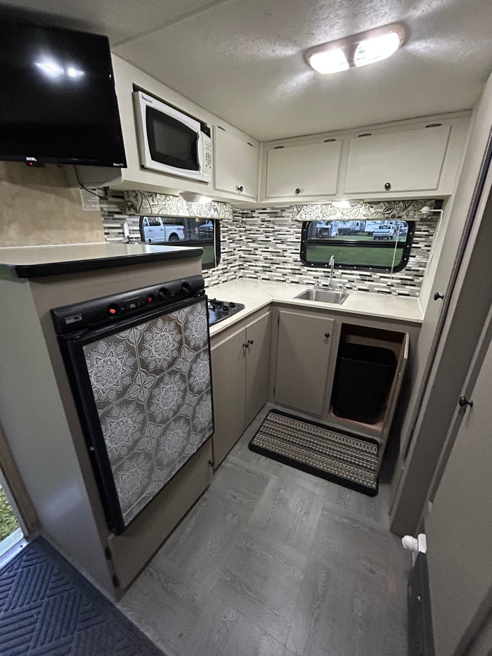 RV rental: Bright kitchen area with TV, microwave, stovetop, decorated fridge, sink, and neat storage.