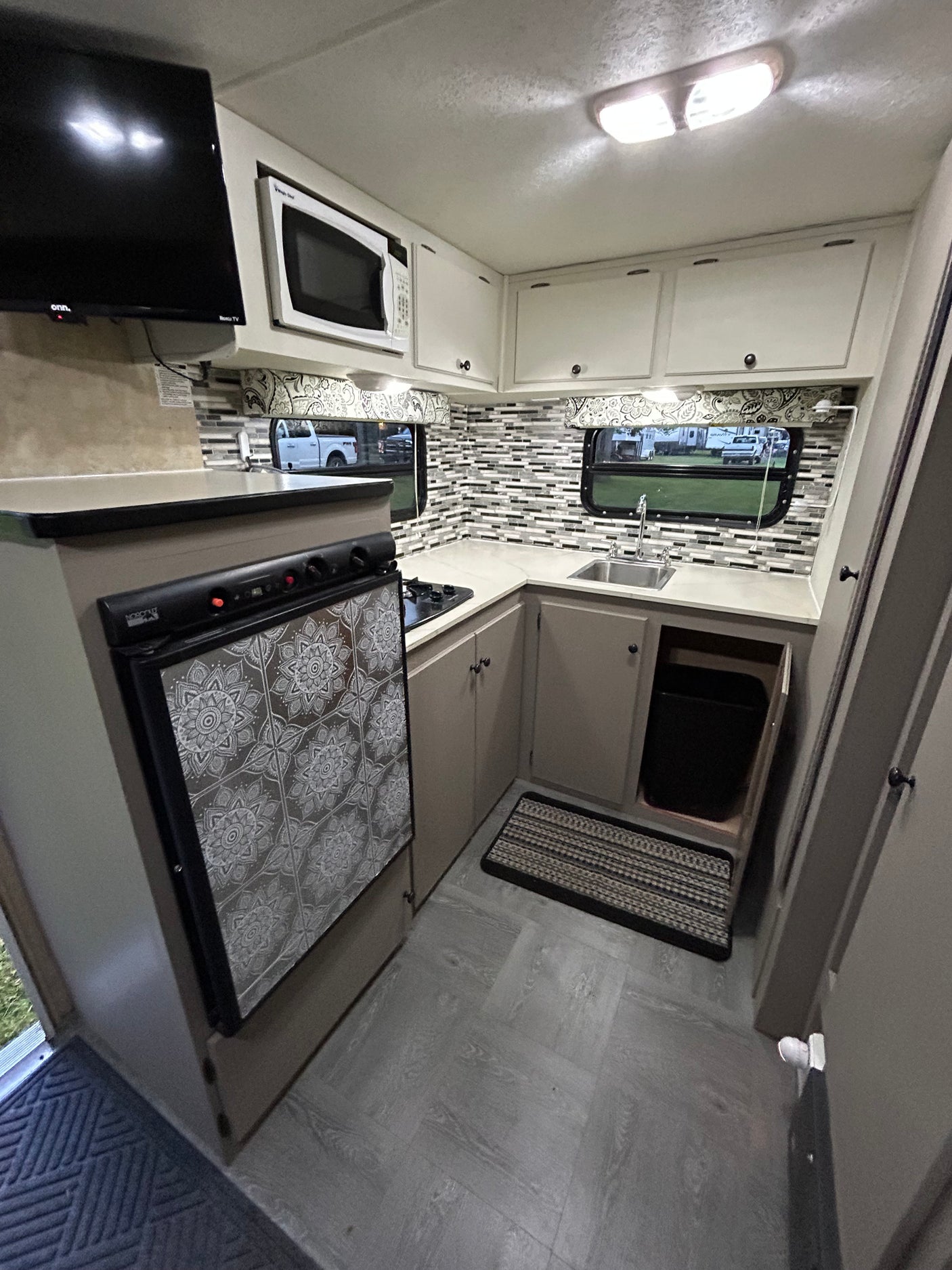 RV rental: Bright kitchen area with TV, microwave, stovetop, decorated fridge, sink, and neat storage.