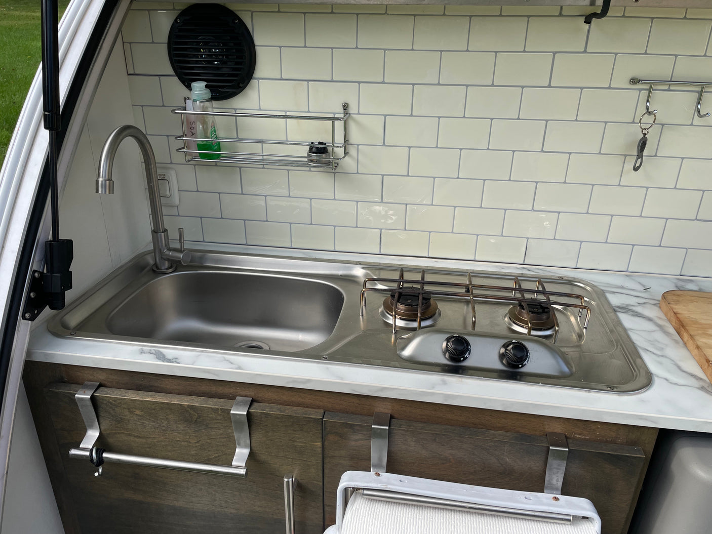 RV rental kitchen: compact stainless steel sink, two-burner stove, and tiled backsplash for convenient travel cooking.