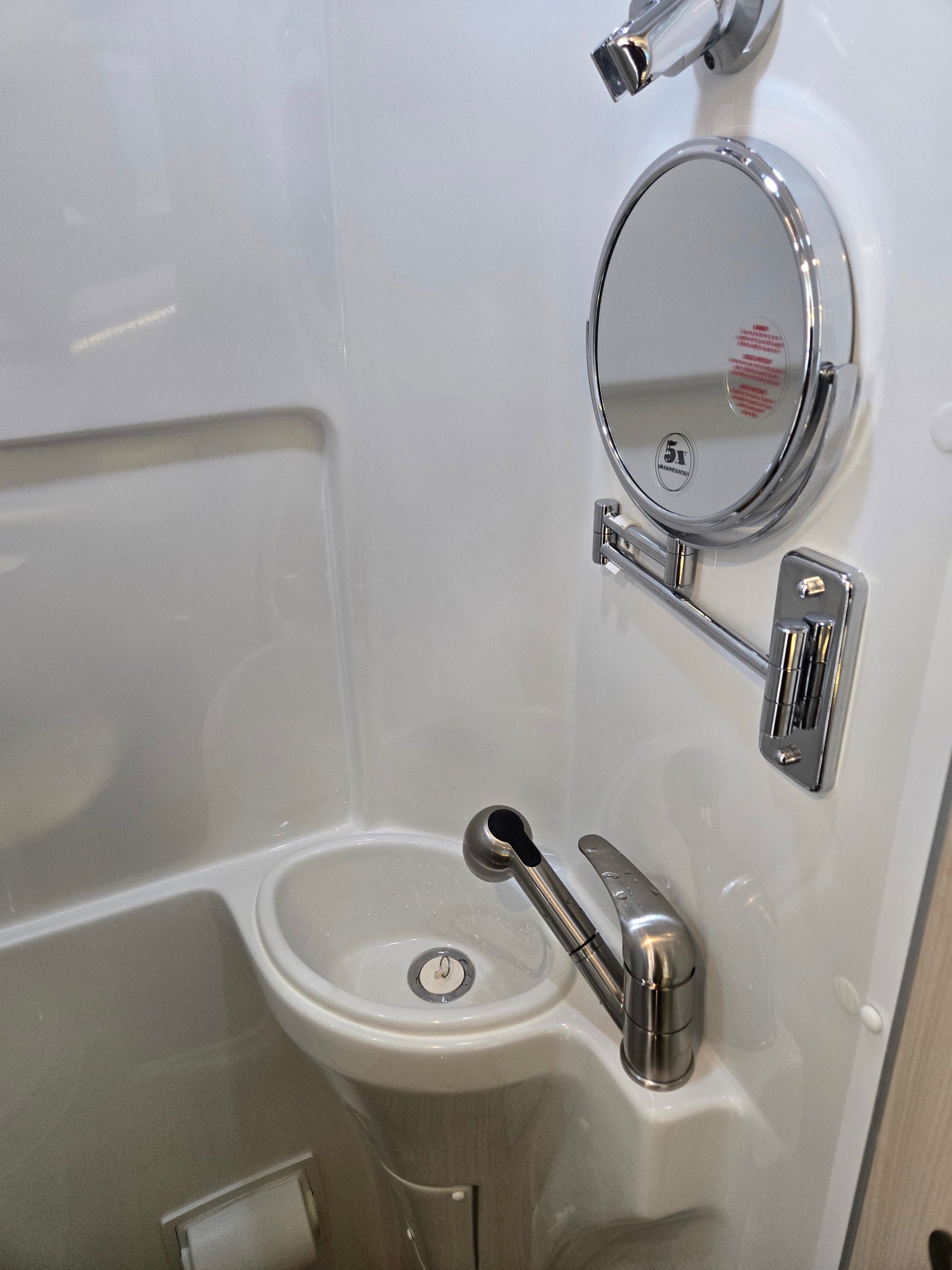 Compact RV rental bathroom with a sink, pull-out faucet, magnifying mirror, and integrated toilet paper holder, ideal for travel.