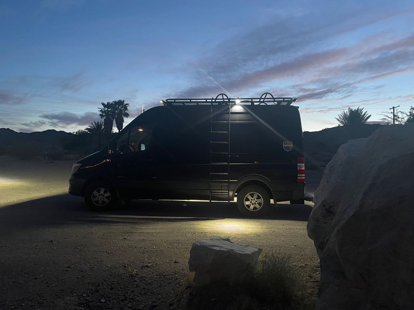 Black Sprinter RV rental in desert at dusk with lights on, ready for adventure.