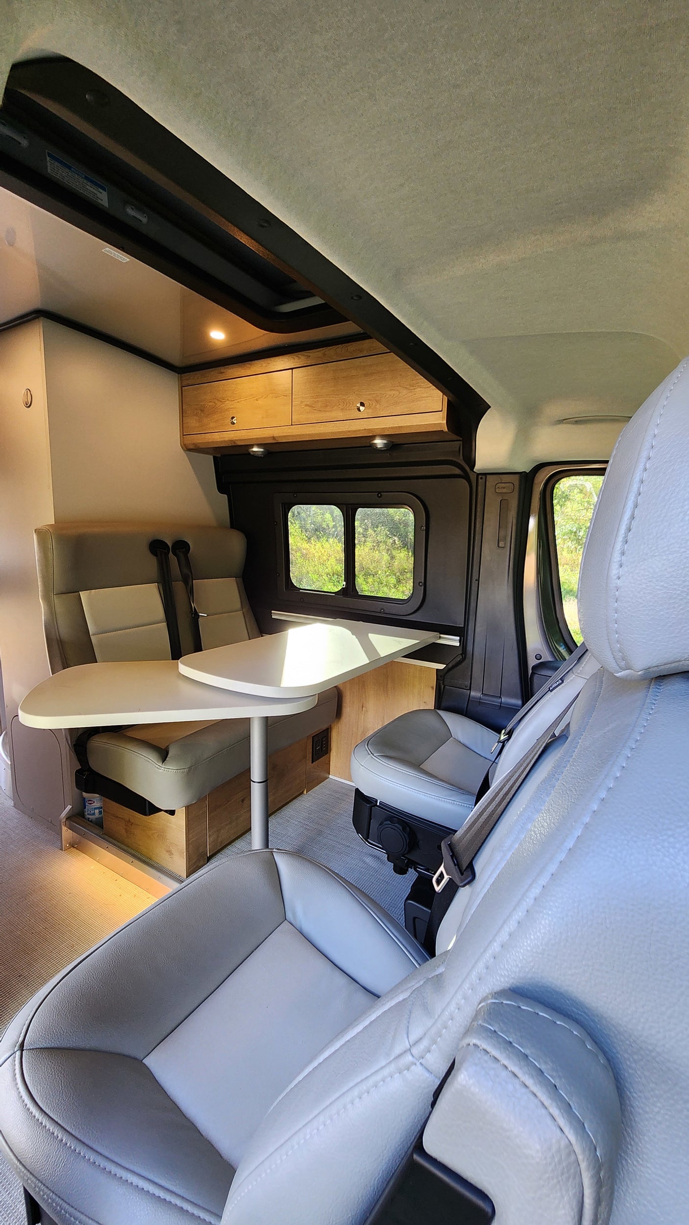 Spacious RV rental interior featuring a light-colored dining table, comfortable bench seating, and wood cabinets.