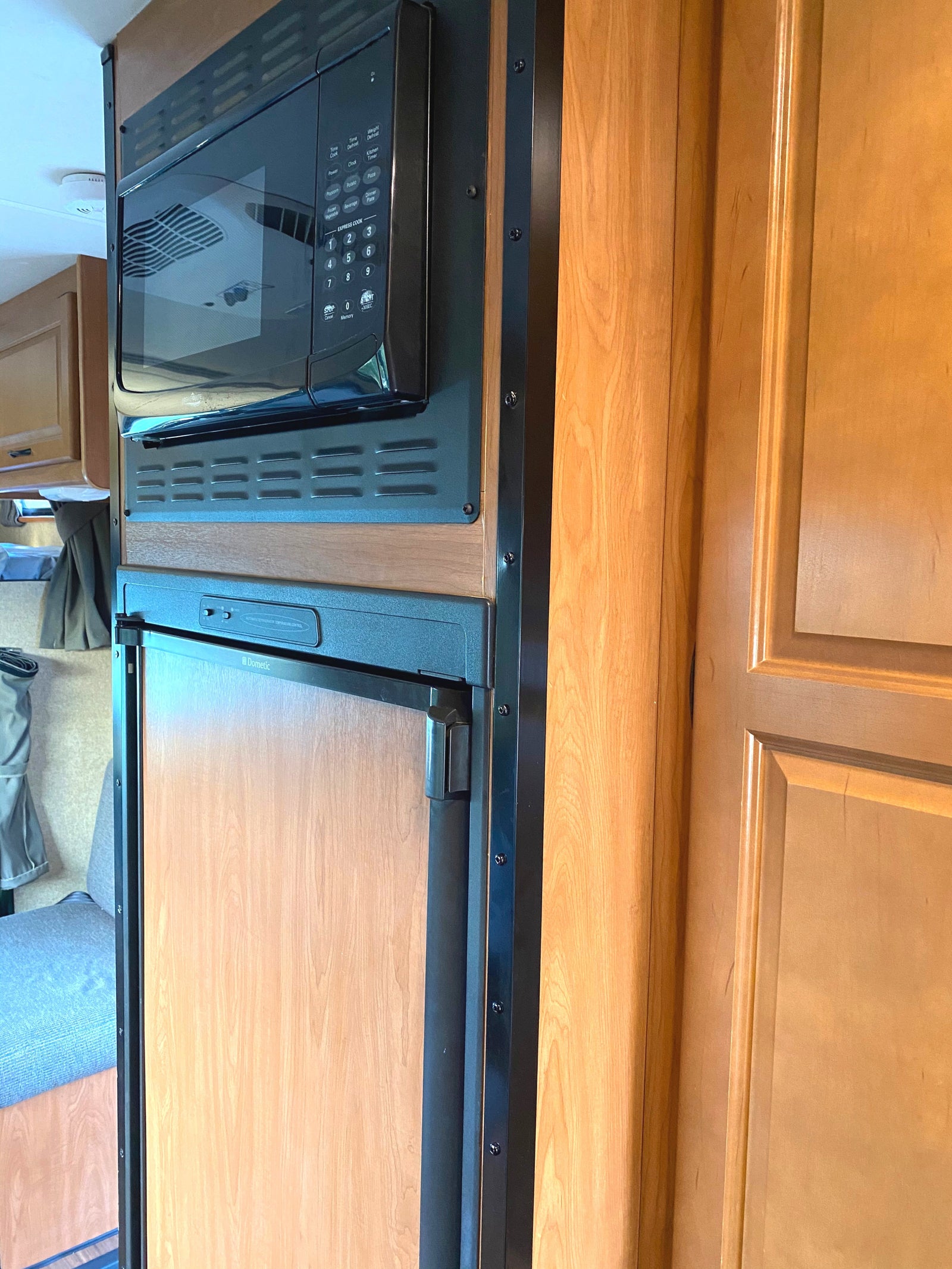 Inside an RV rental: compact microwave above Dometic refrigerator with wood finishes.