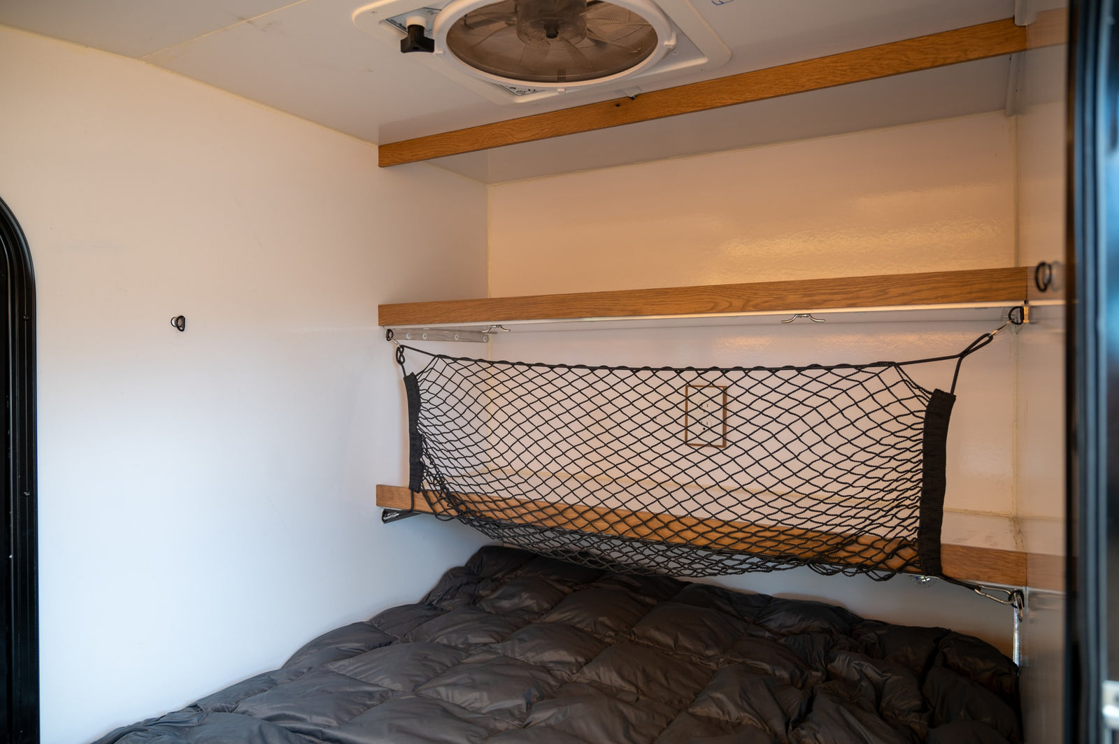 Cozy RV rental interior with a bed, overhead shelf, and practical cargo net storage.