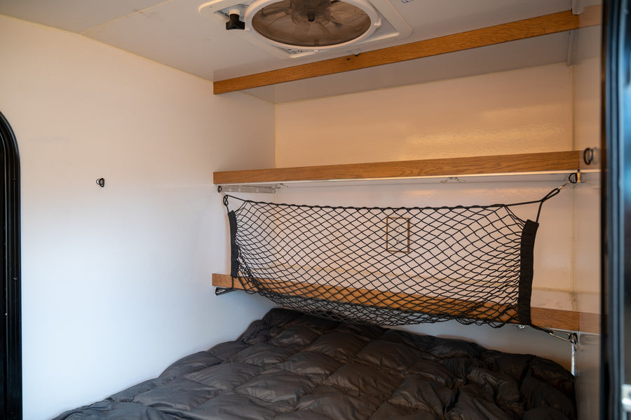 Cozy RV rental interior with a bed, overhead shelf, and practical cargo net storage.