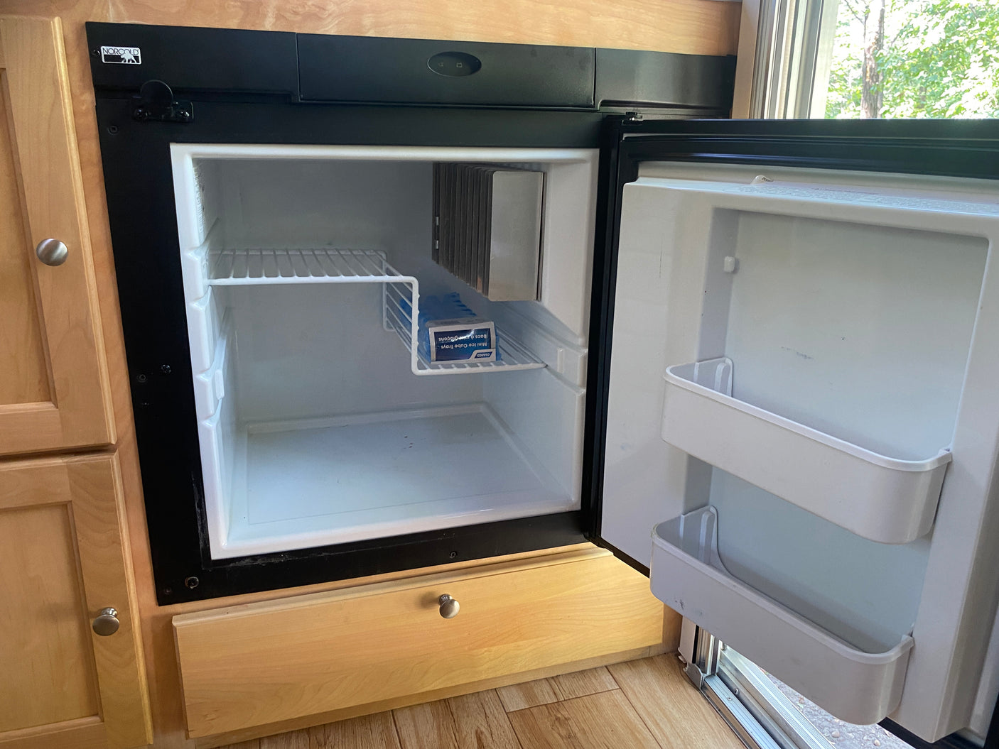 Inside an RV rental: a compact Norcold refrigerator, open to show its white interior, shelves, and ice cube trays.