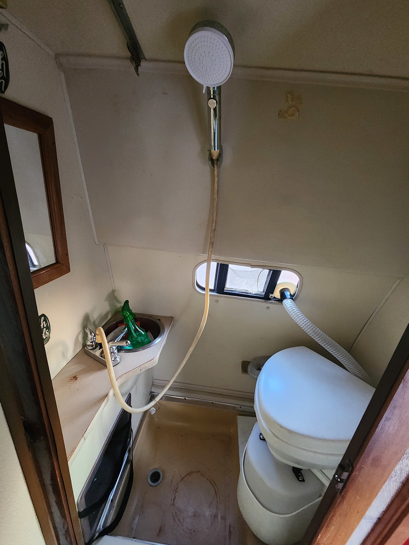 Compact RV rental bathroom with a sink, handheld shower, window, and composting toilet inside.