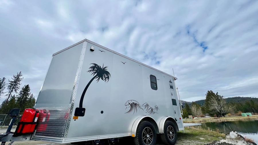 This unique custom RV rental, adorned with coastal decals, sits by a serene lake, ready for adventure.