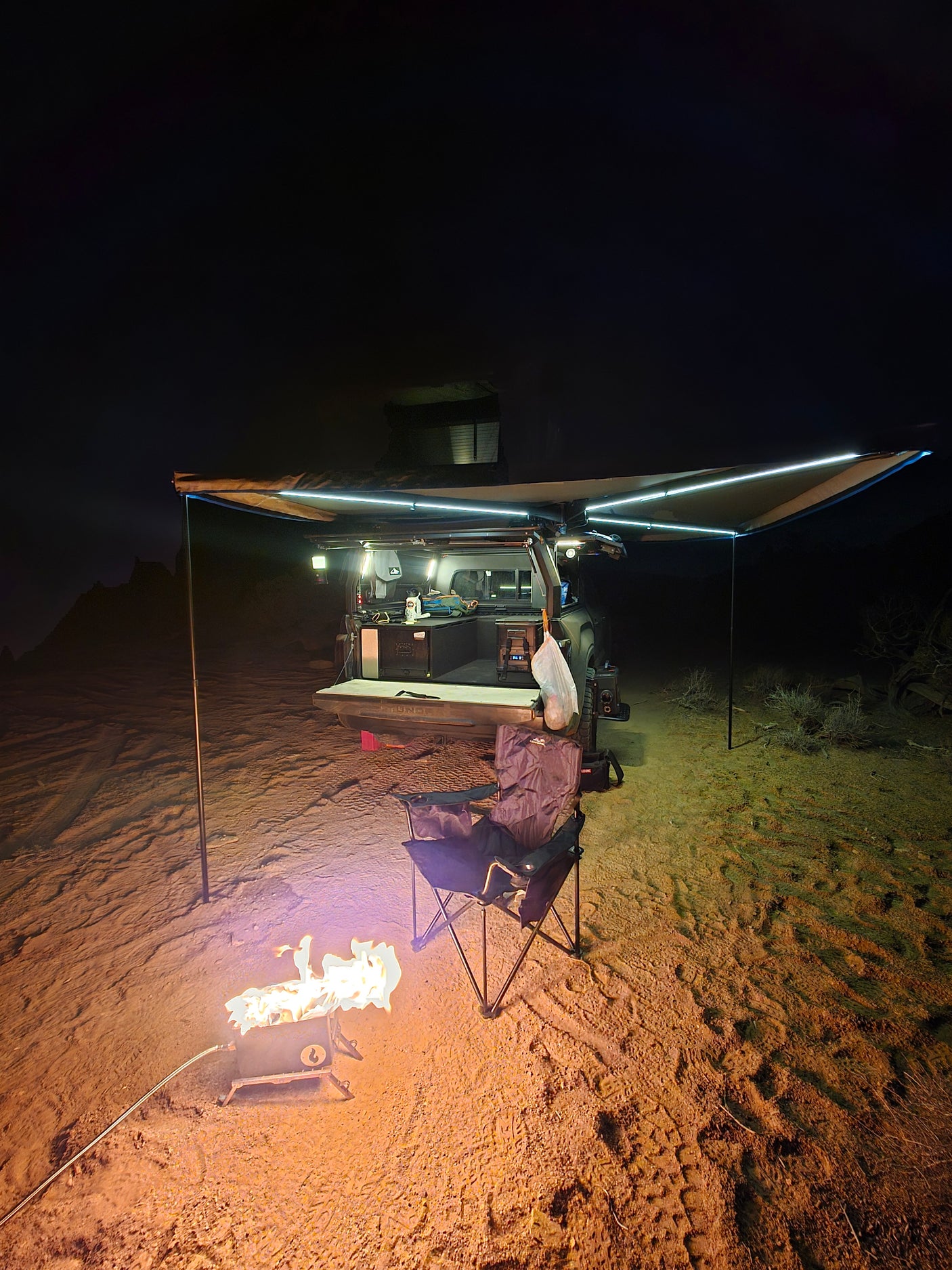 Night desert scene: an rv rental overland setup with illuminated awning, cozy campfire, and camping chair ready.