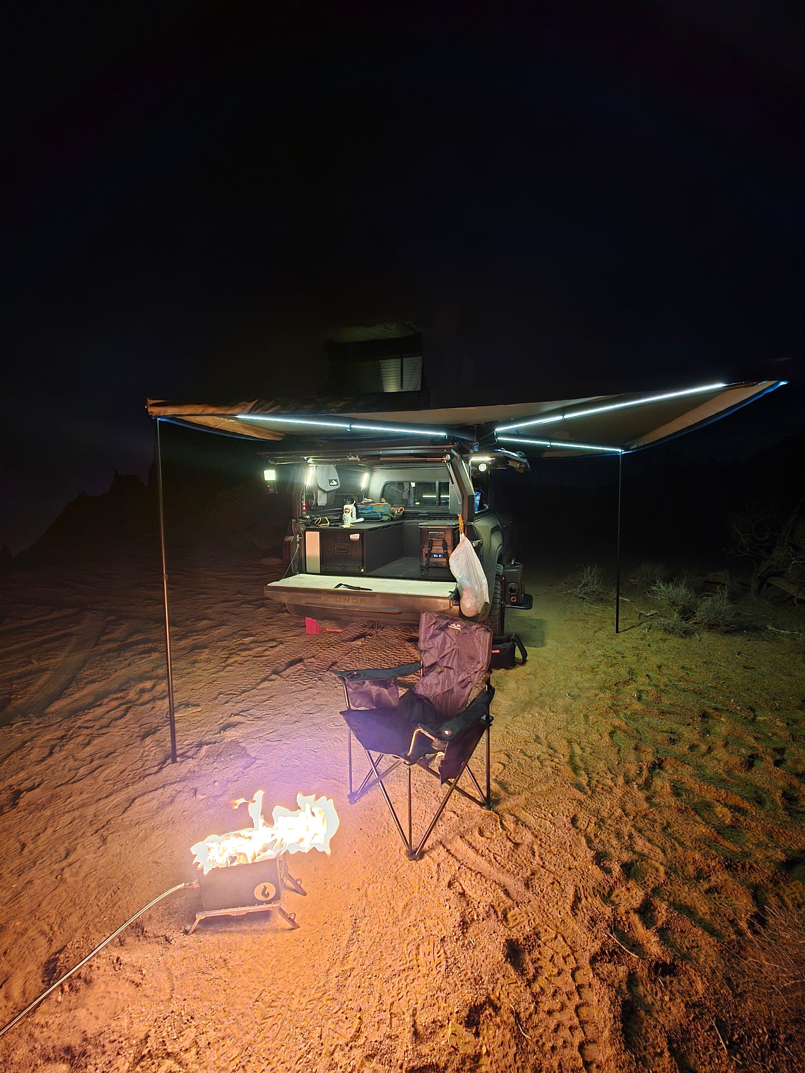 Night desert scene: an rv rental overland setup with illuminated awning, cozy campfire, and camping chair ready.