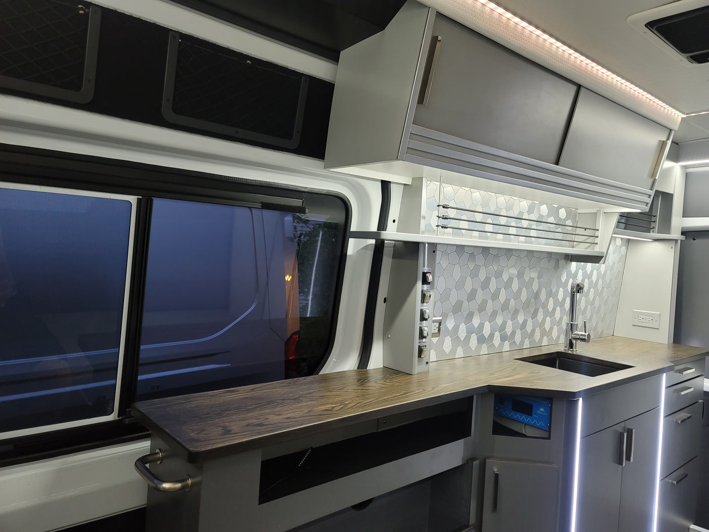 Spacious rv rental interior features a modern kitchen with a wooden countertop, sink, geometric backsplash, and ample storage.